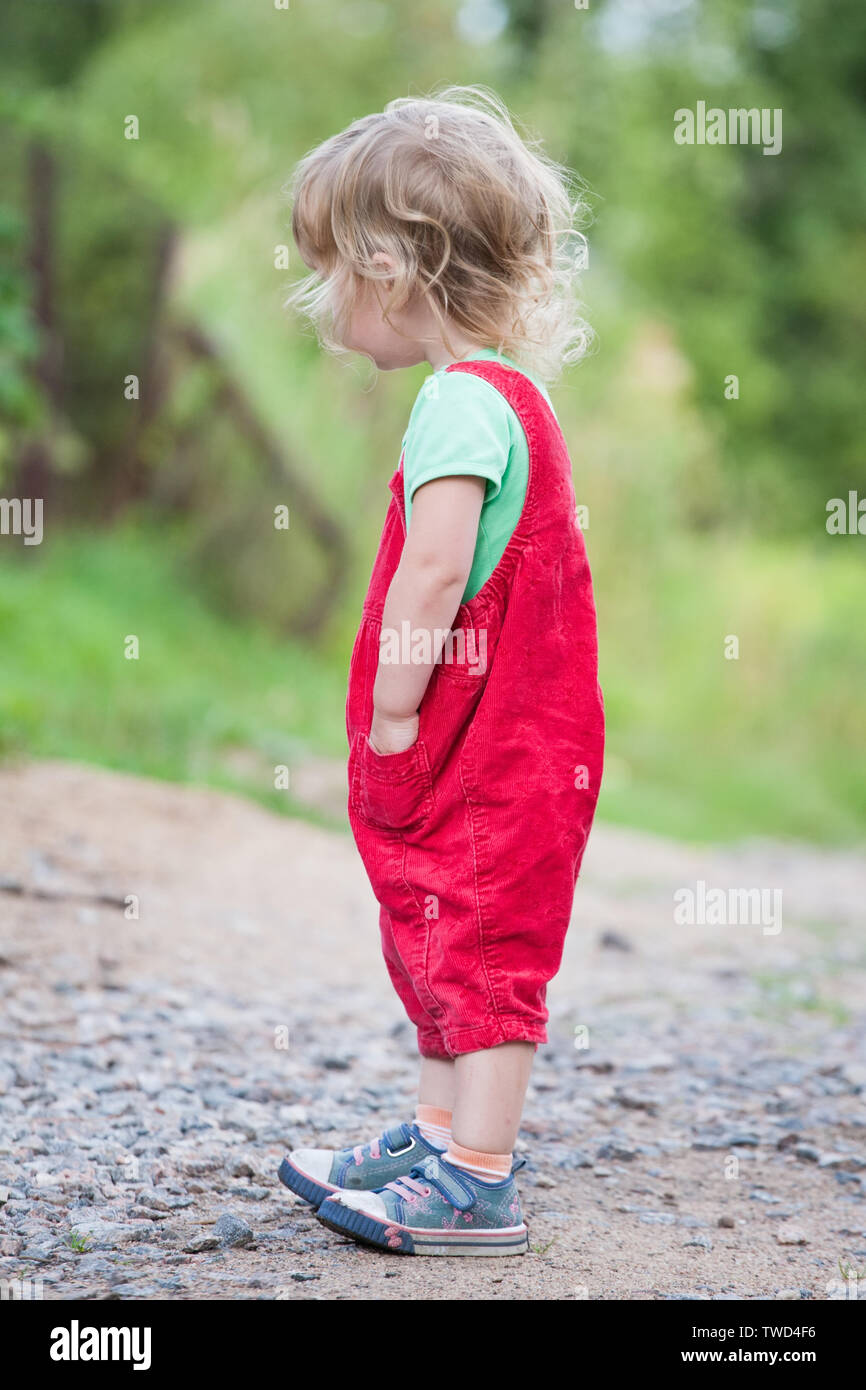 cute kid girl in red pants standing tall on summer outdoor background Stock Photo