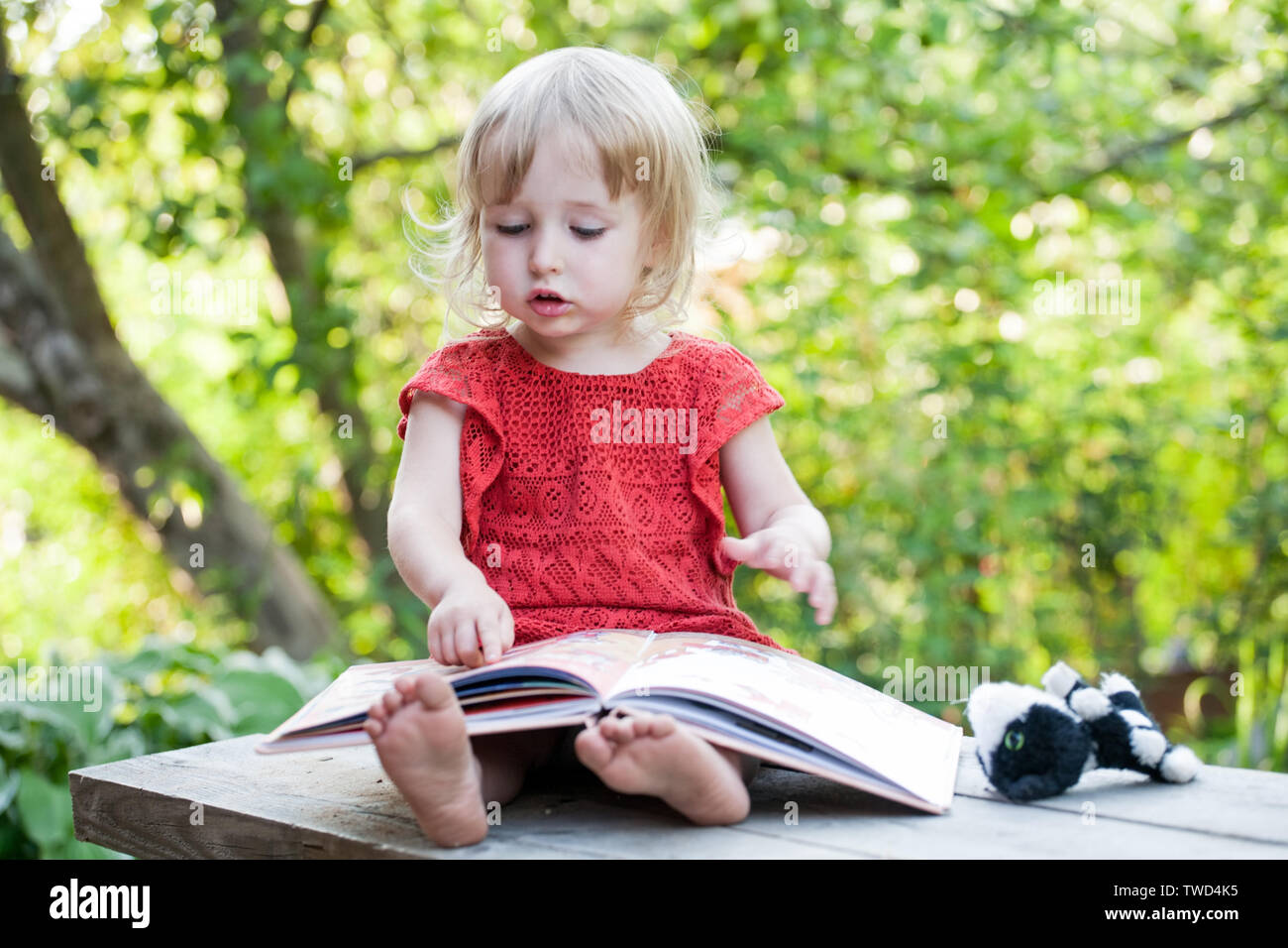 kid girl sitting with big book on summer outdoor background Stock Photo