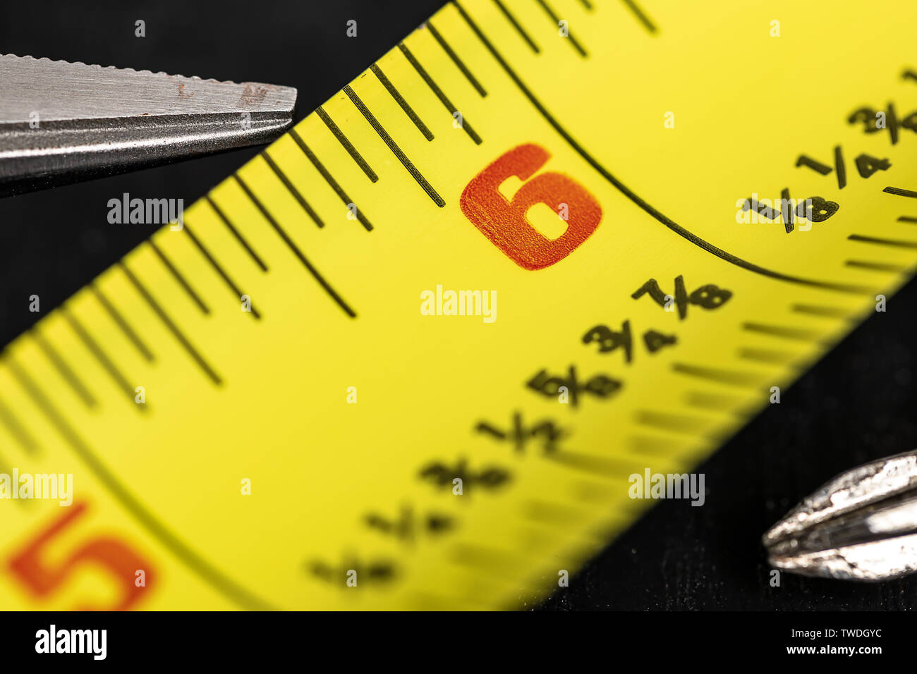 A macro image of a yellow Tape Measure at the 6 inch mark, 1/8 inch hashes are labeled and center of focus in center frame a needle nose plier and a s Stock Photo