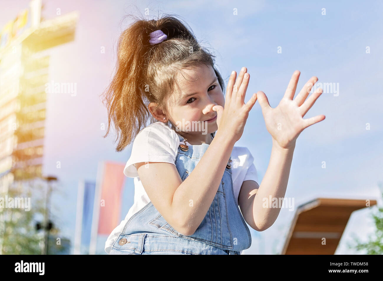 Cute happy Caucasian girl in denim overalls grimacing on sky background. Cheerful emotion. Lifestyle Stock Photo