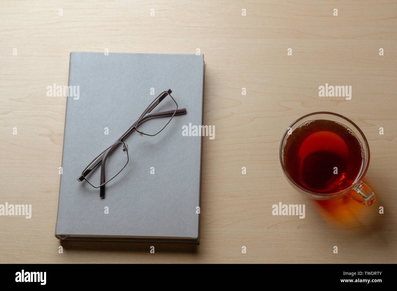 Gray diary, cup of tea, and glasses on a brown table, top view Stock