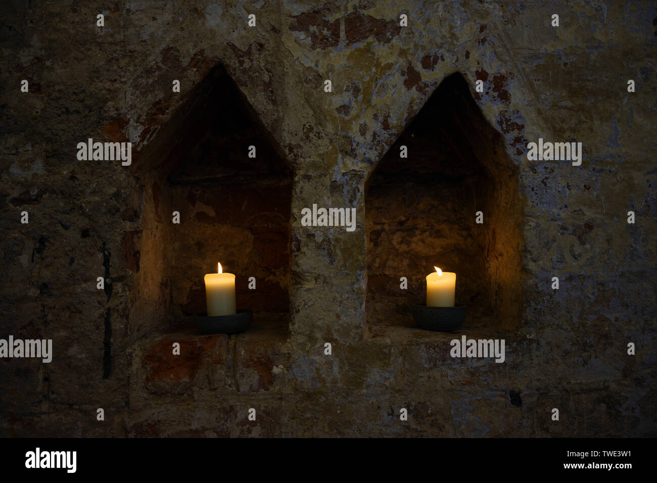 two white burning candles in two niches in a dark old brick wall of a