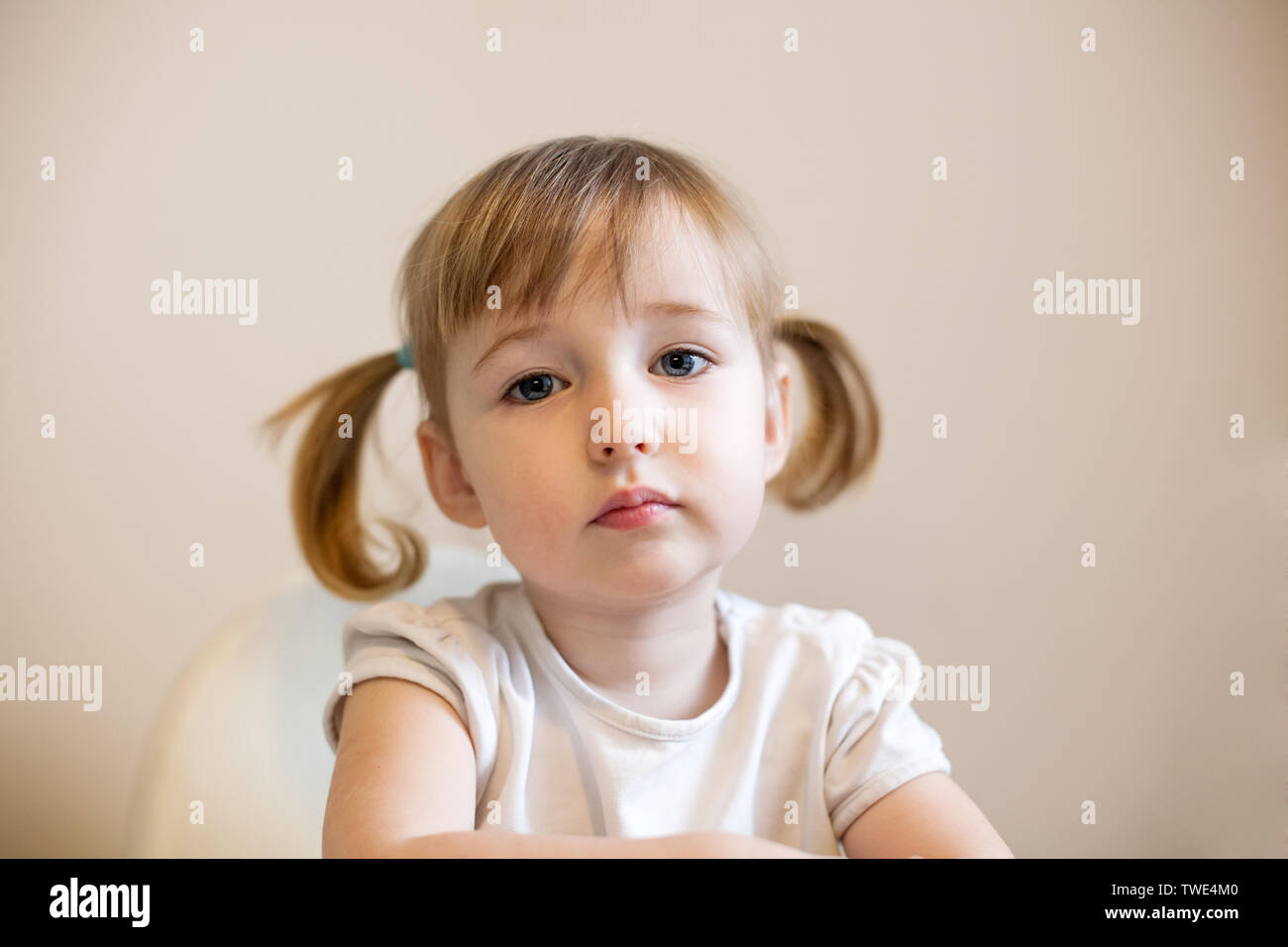 little kid Caucasian girl face closeup cute portrait with pigtails on plain background Stock Photo