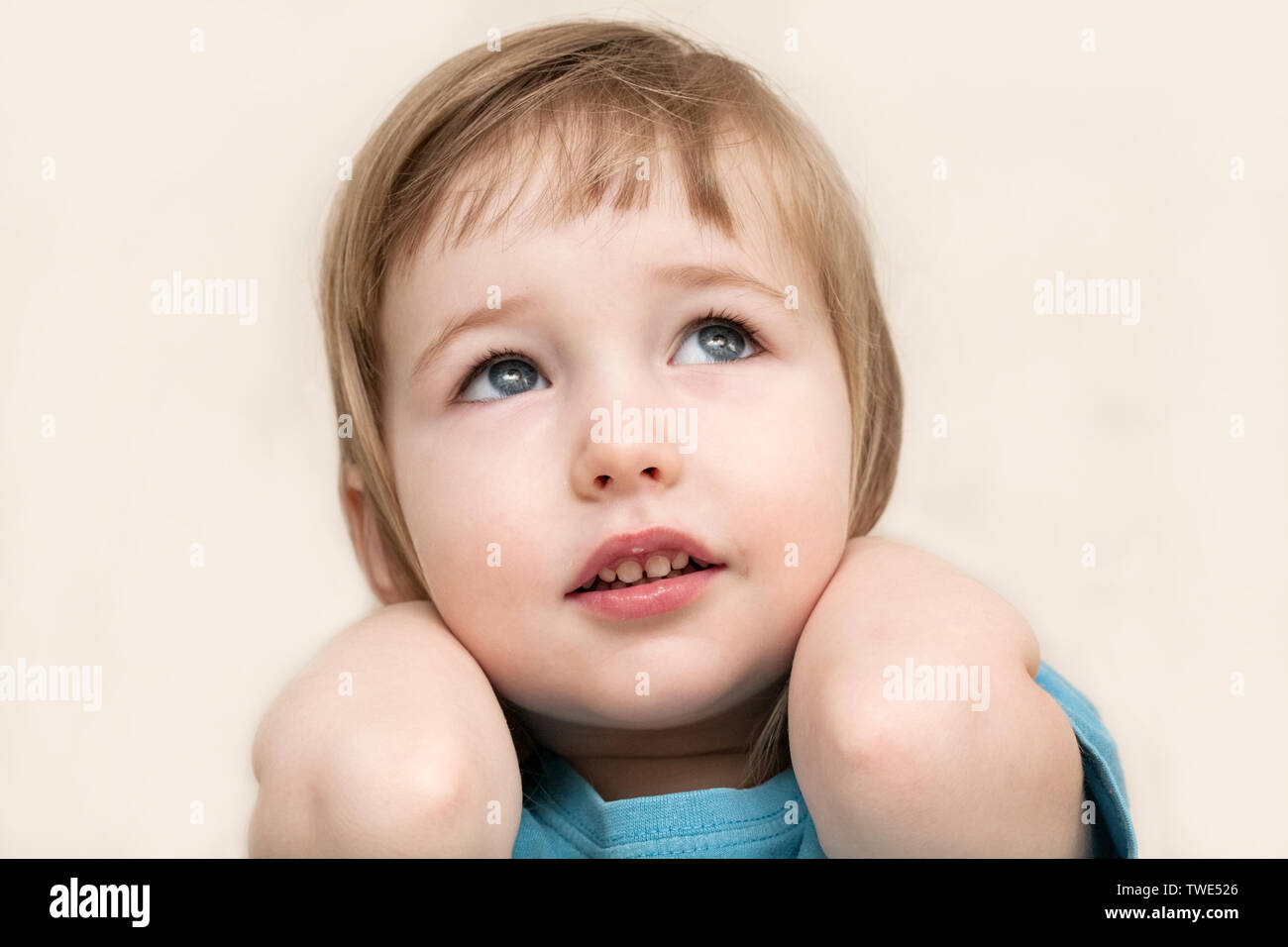 funny pensive emotional white child girl face closeup on beige wall background Stock Photo