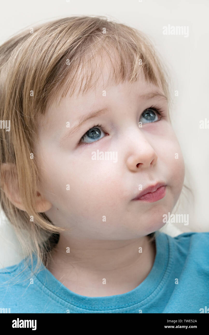 funny serious emotional white child girl face closeup on beige wall background Stock Photo