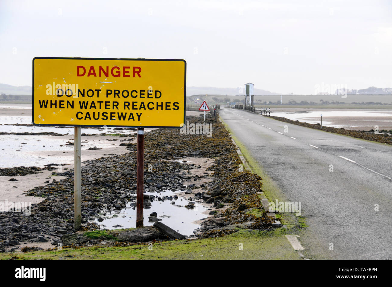 The Danger warning sign for tourist traffic crossing the 3-mile stretch of tarmac road at low tide connecting Lindisfarne Holy Island from the mainland Stock Photo