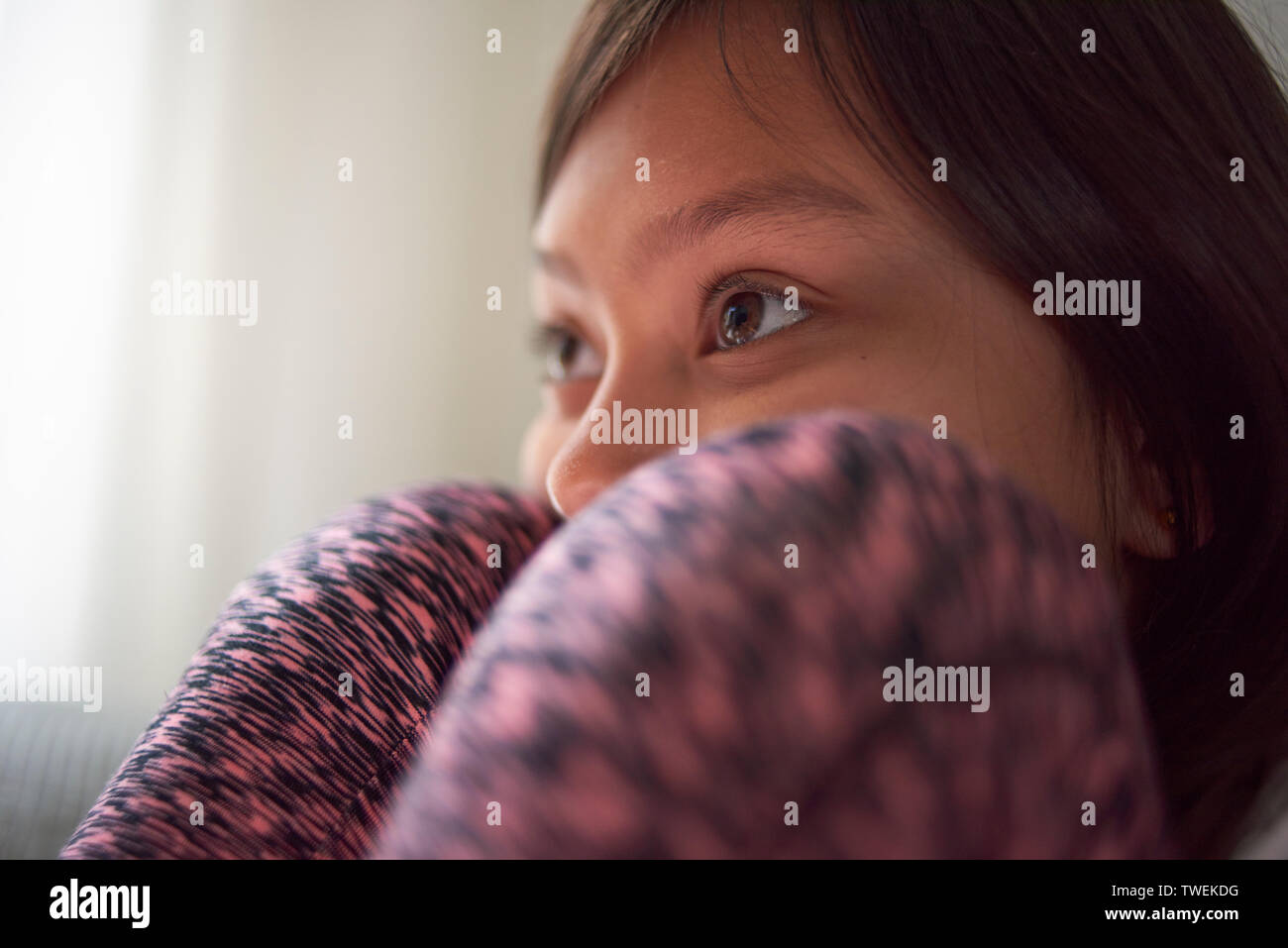 Young Asian girl sitting at home on the sofa with her head between her knees watching television Stock Photo