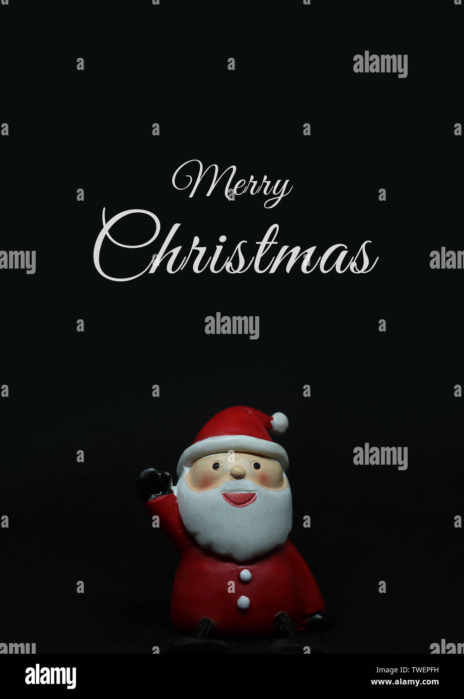 Adorable santa claus doll on black background with white Merry Christmas text above. Stock Photo