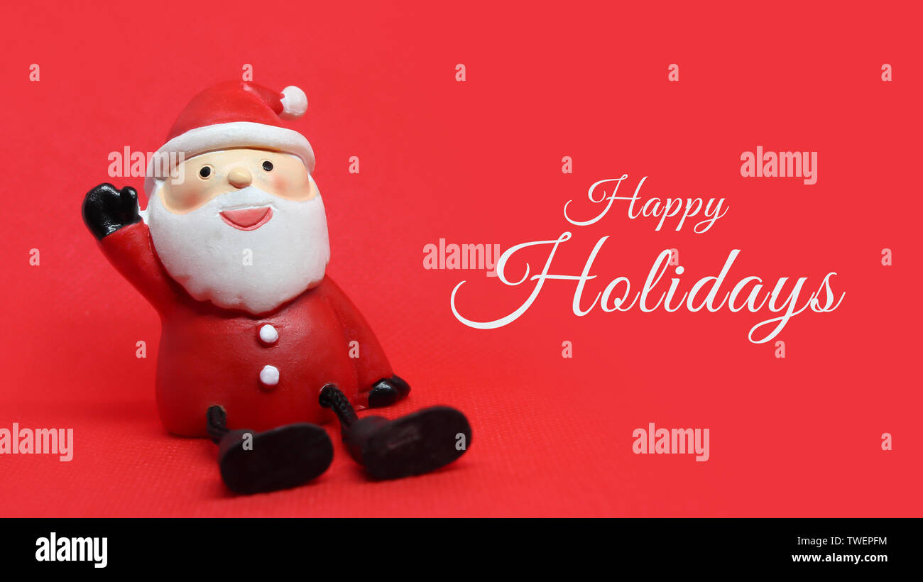 Adorable santa claus doll on red background with white Happy Holidays text to the right. Stock Photo