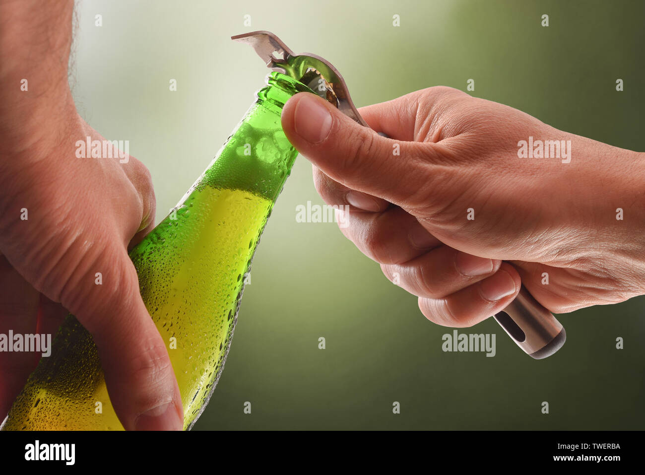 opening a green glass bottle with a metal bottle opener and green background.  Horizontal composition. Front view. Stock Photo