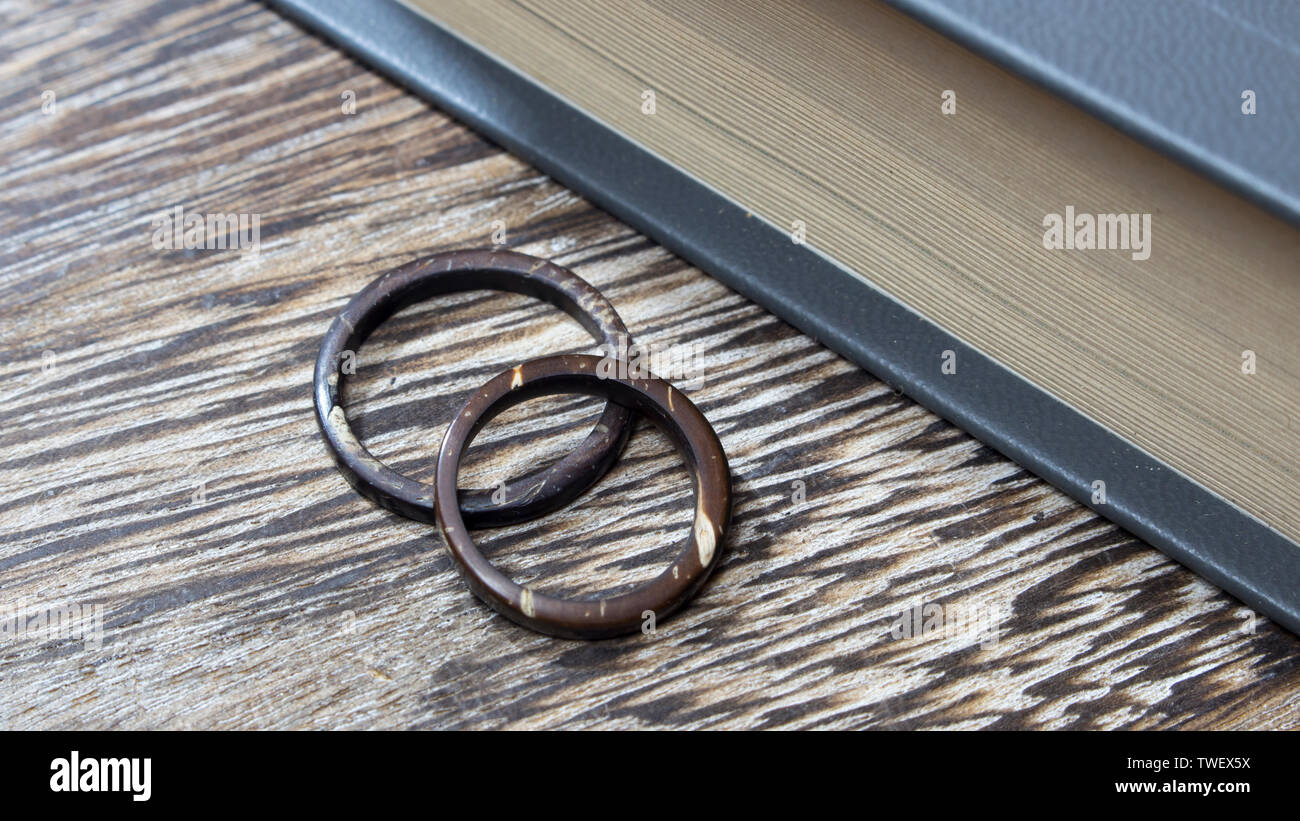 Unique handmade coconut rings in wooden background with book edge. Artisan wedding ring bands. Love and union concept. Stock Photo