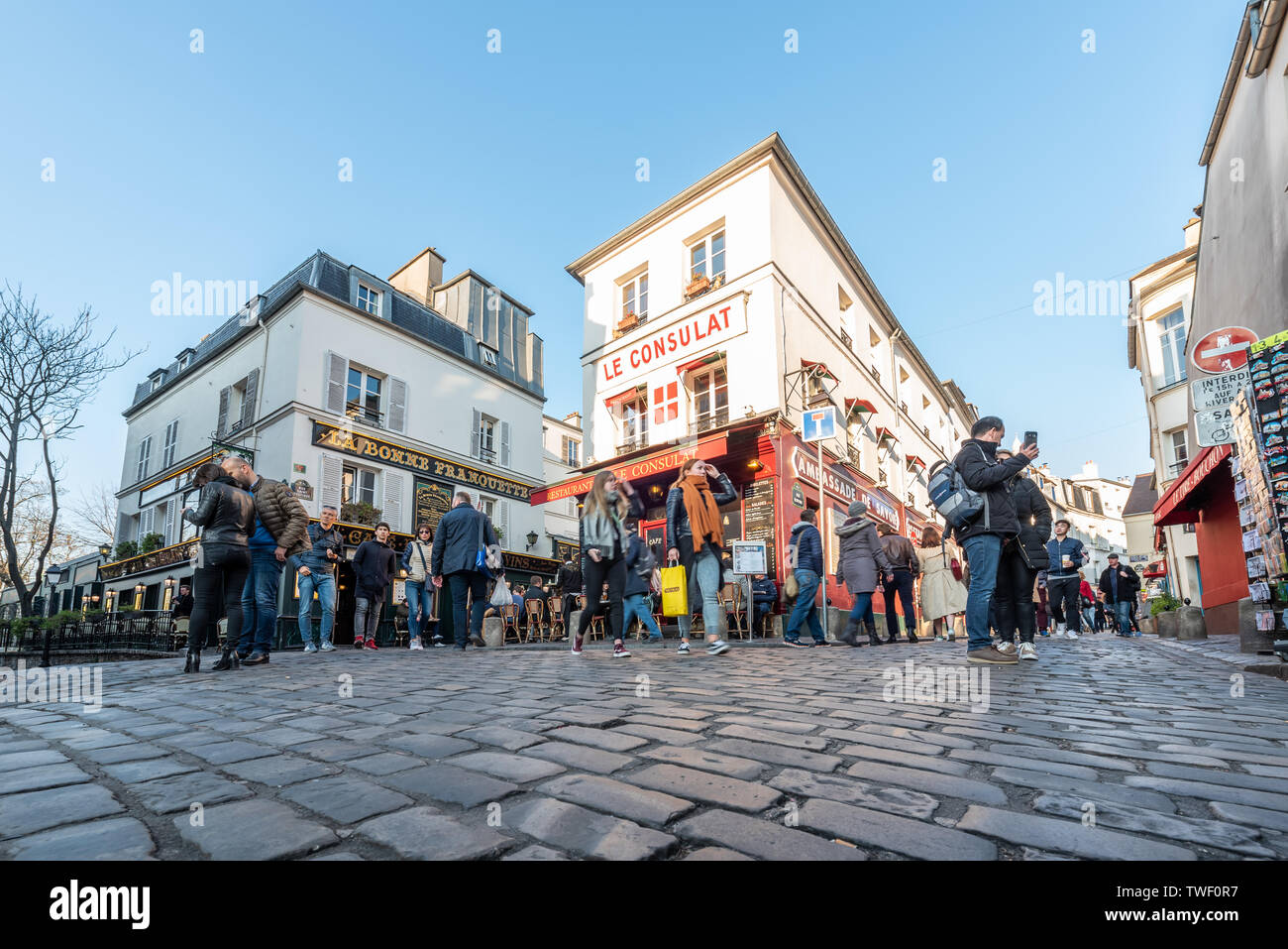 Paris, France - April 12, 2019 : People sitting at the terrace of Le consulat restaurant in Montmartre in the evening on a sunny day with cobblestones in the foreground Stock Photo