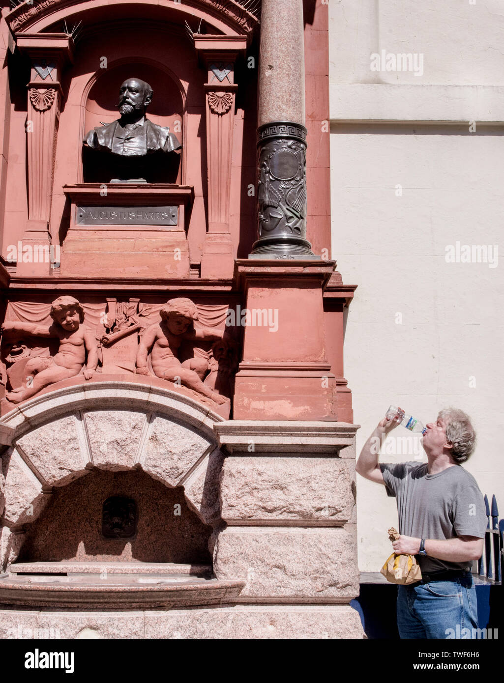 Man looking up at statue whilst drinking bottled water in London. Stock Photo
