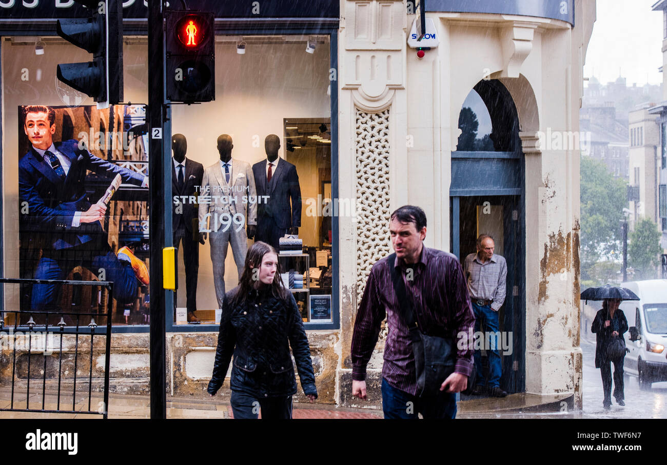 Man and woman crossing road in heavy rainstorm with man in background sheltering in shop doorway in Harrogate in North Yorkshire. Stock Photo