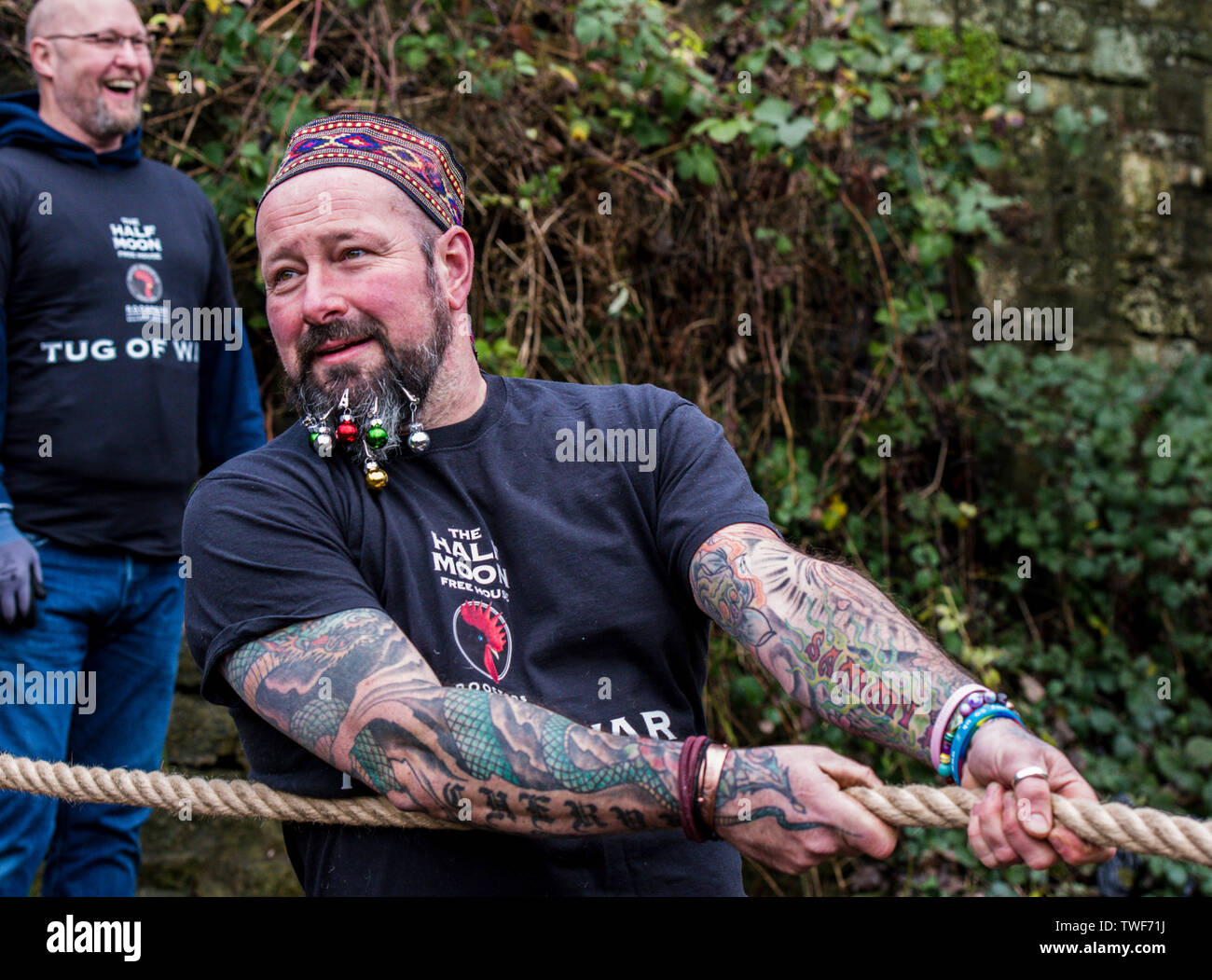 Tattooed man with Christmas baubles in his beard competing in the traditional Boxing Day Tug of War between the banks of the River Nidd. Stock Photo