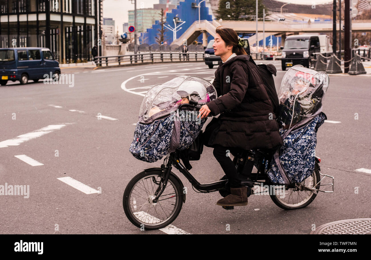 Woman riding bike with toddler seats attached to the back and front of