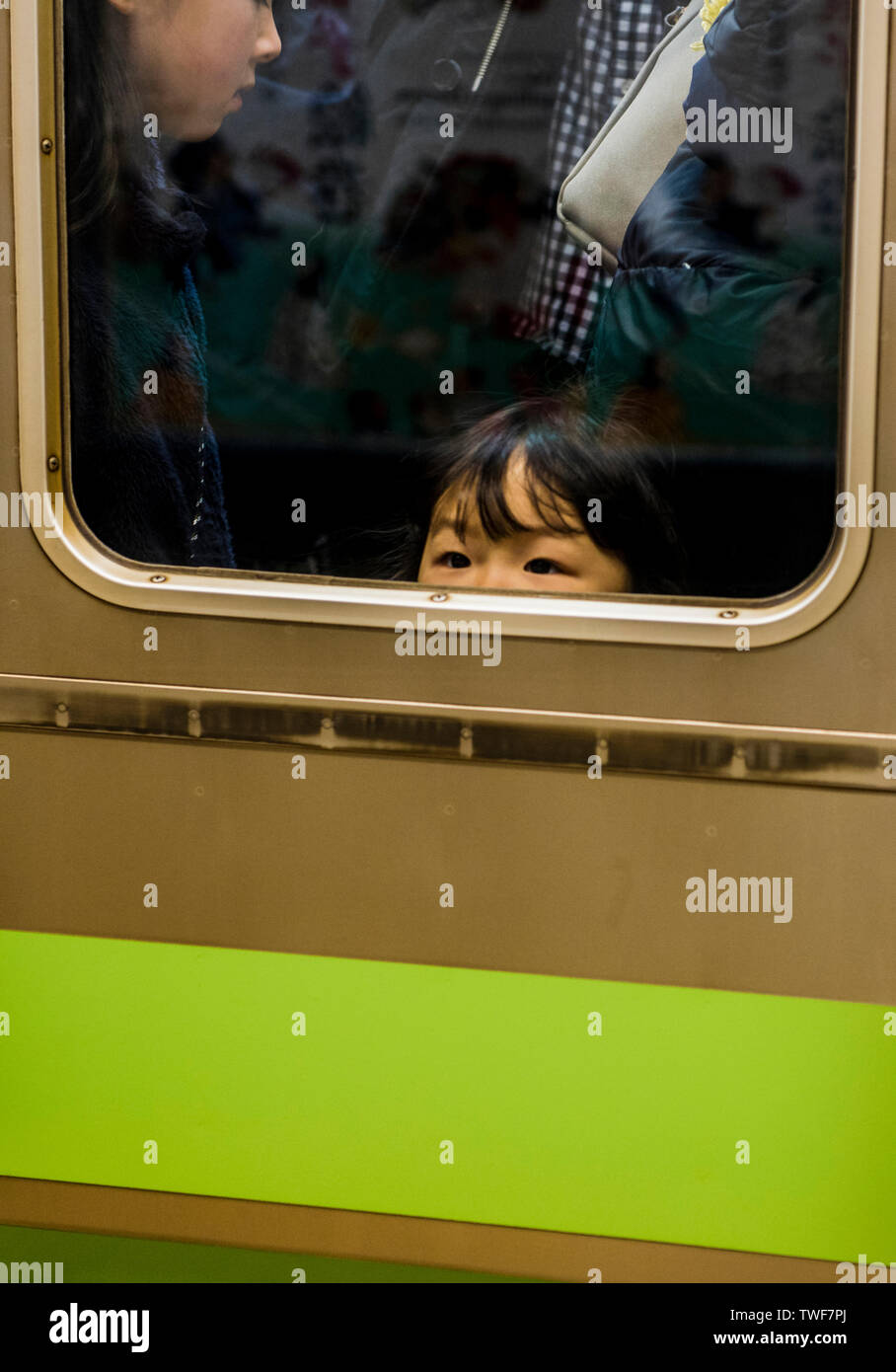 Young girl peering out of busy train window in Tokyo in Japan. Stock Photo
