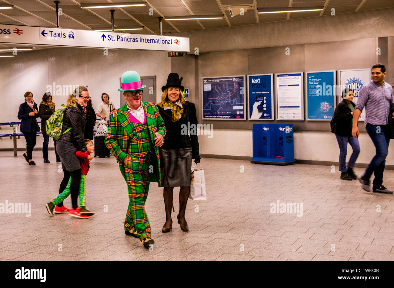 Couple dressed in extravagant clothing walking through Kings Cross underground station in London. Stock Photo