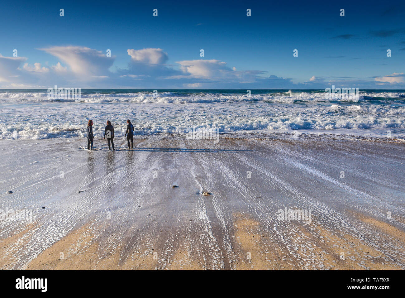 People in wetsuits standing on the shoreline at Fistral Beach in