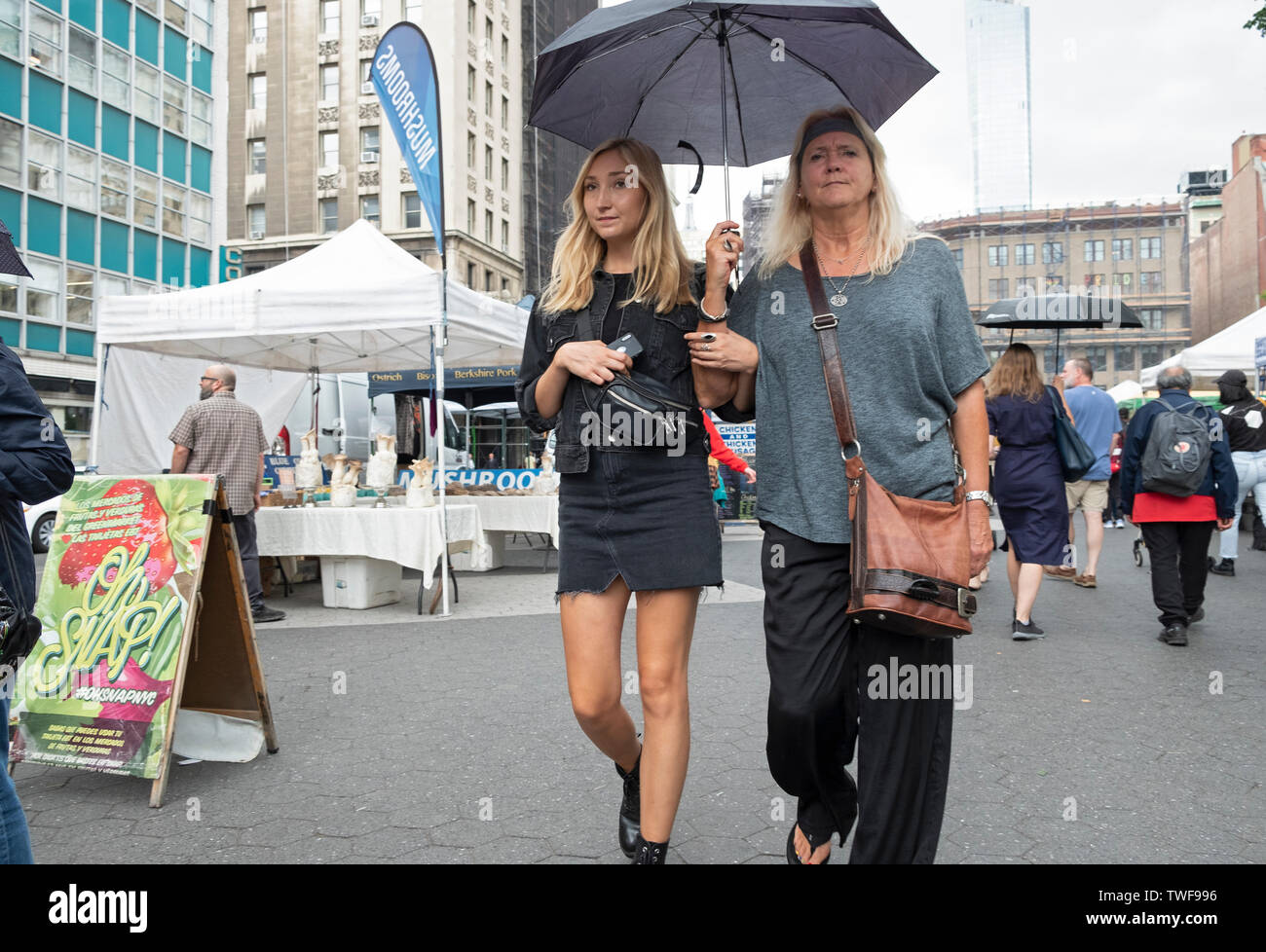 Two women who appear to be mother & daughter, share an umbrella while walking through the Union Square Green Market in lower Manhattan, New York City. Stock Photo