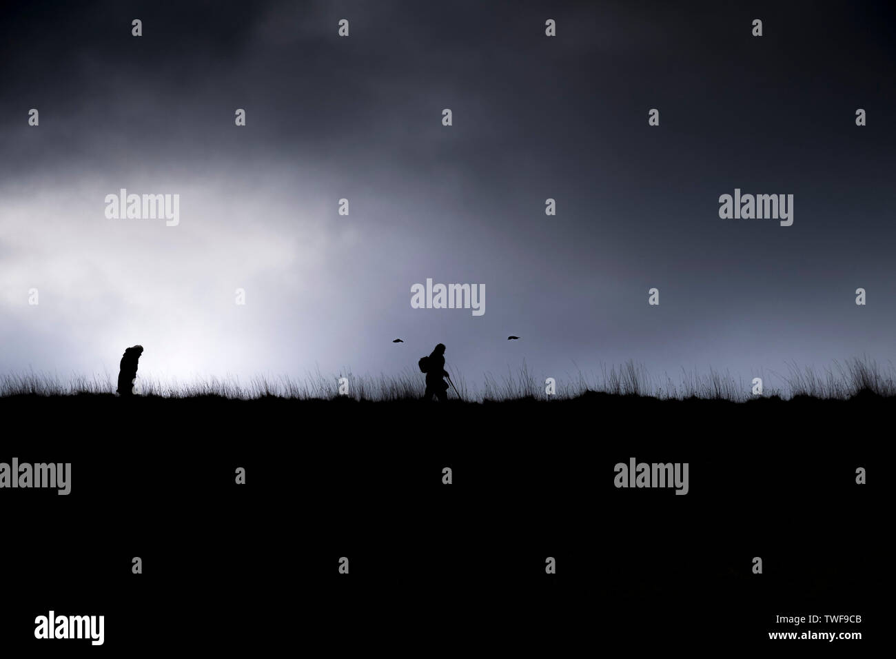 Walkers silhouetted against a brooding stormy sky. Stock Photo