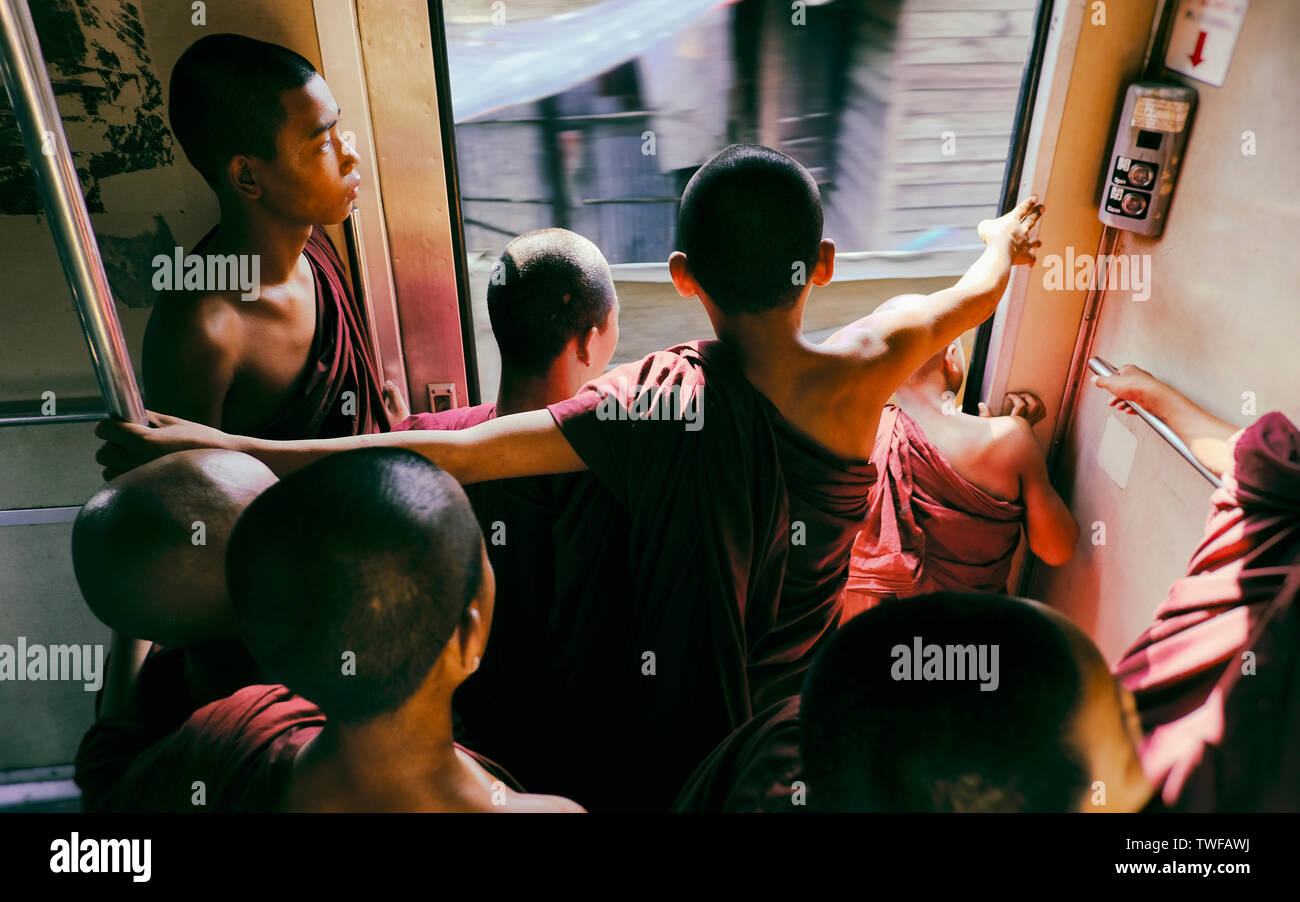 Young Buddhist monks stand looking out of a busy moving train in Yangon. Stock Photo