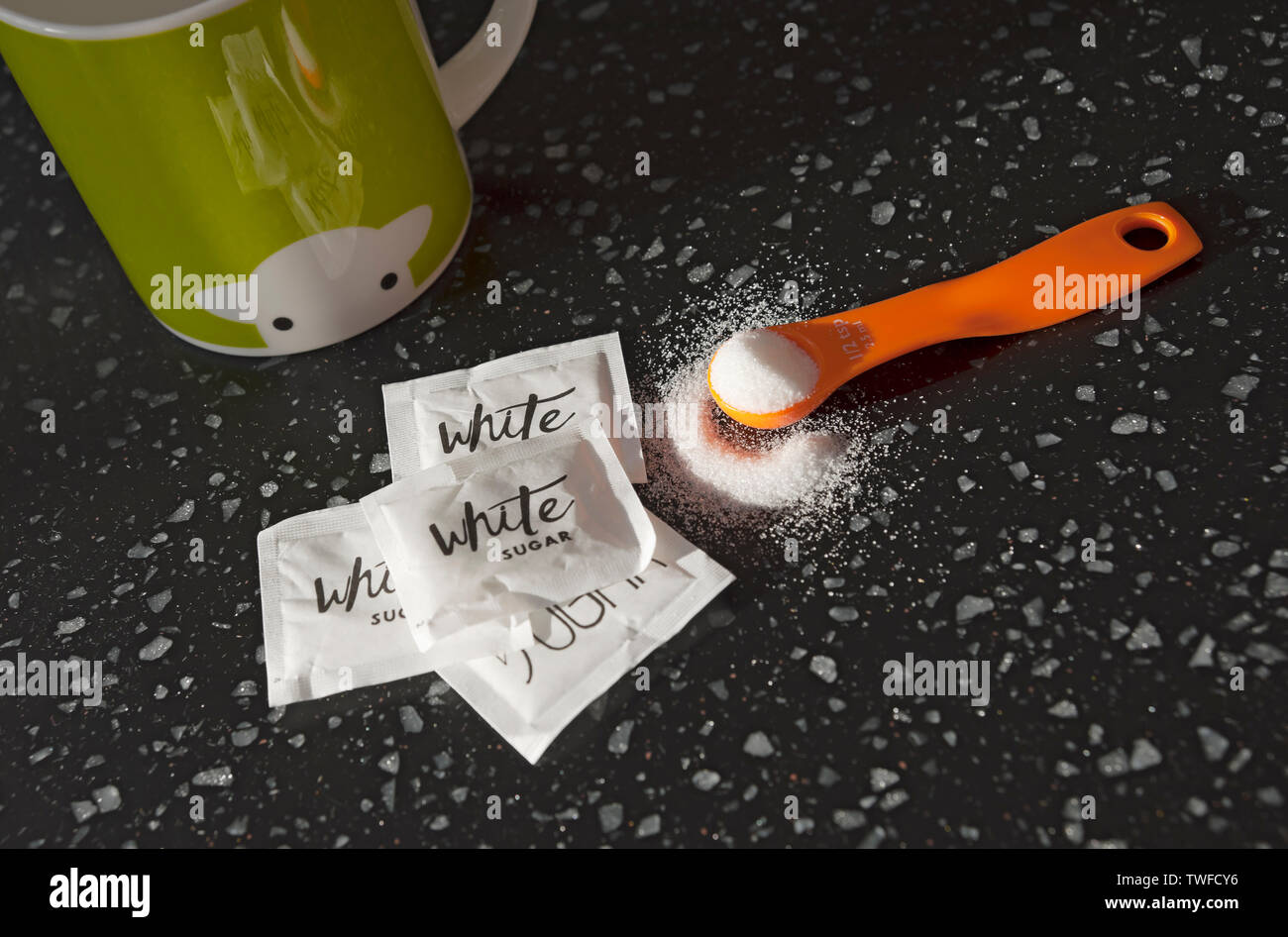 Close up of spoonful of white sugar and sugar sachets. Stock Photo