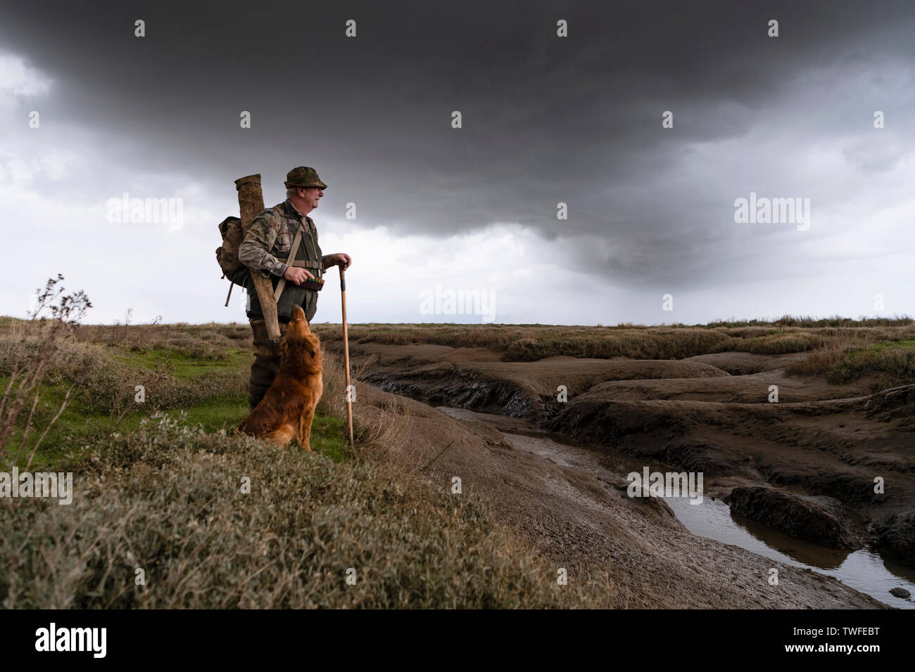 Wildfowling on the Lincolnshire Wash with shooter and gundog walking through the marshes with storm clouds and rain. Stock Photo