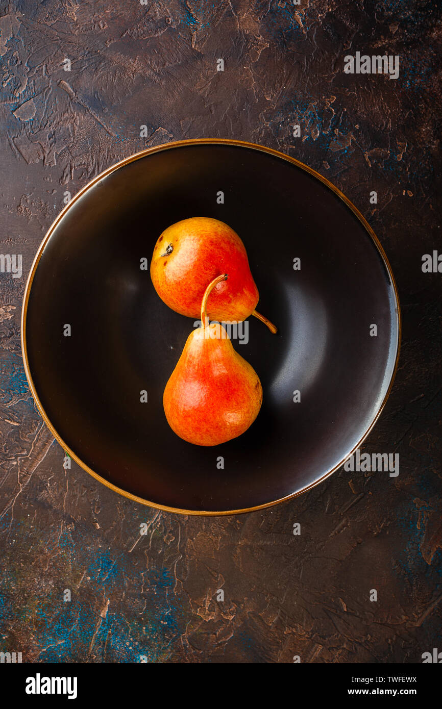 Fresh red-yellow pears on a plate on brown table, top view Stock Photo