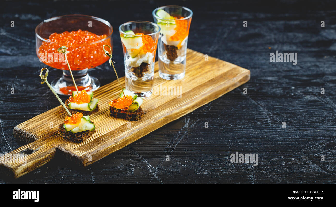 Delicious canapes with red caviar and portioned snacks with caviar and cucumber in glasses. Stock Photo