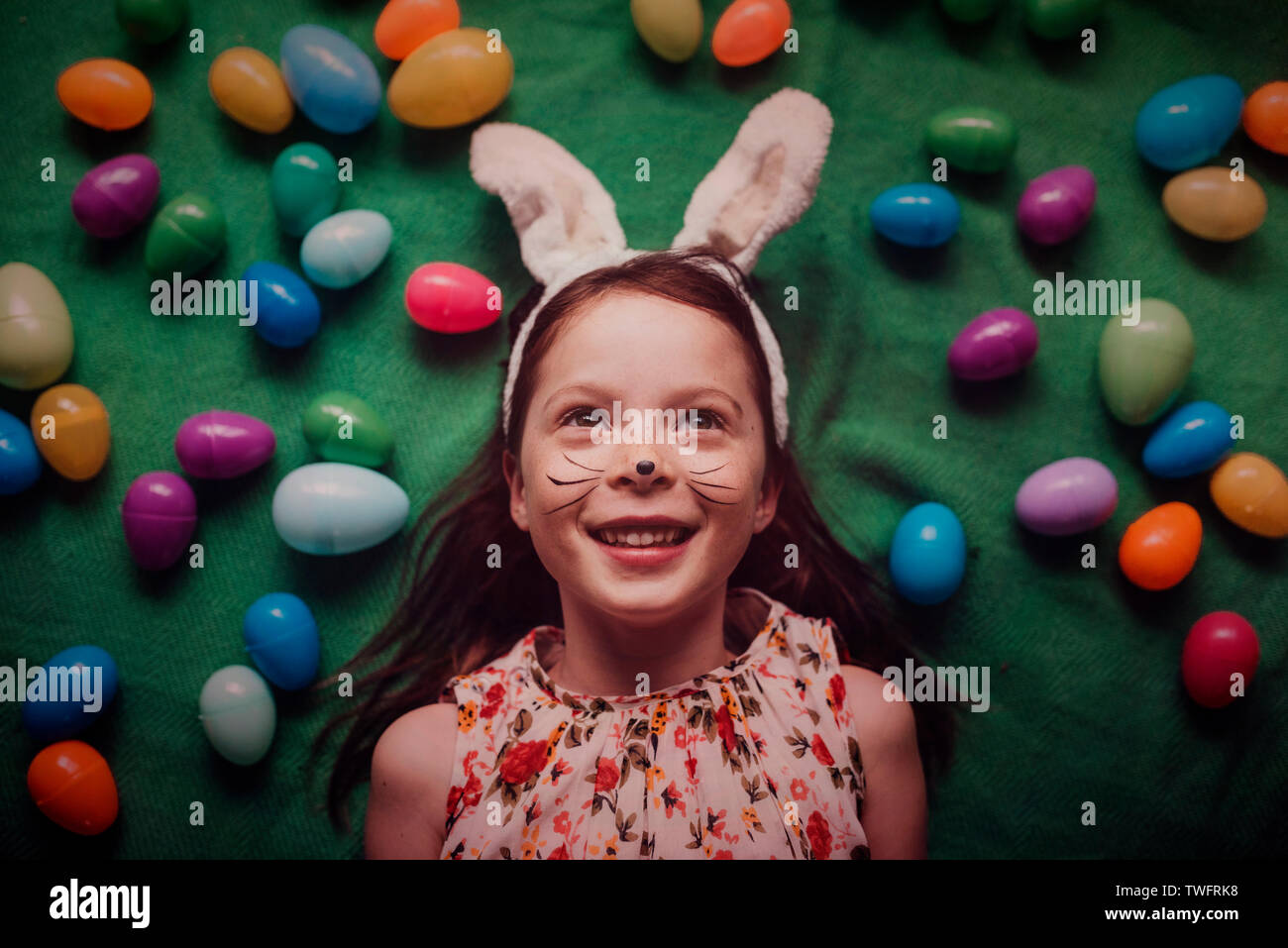 Overhead portrait of young girl wearing bunny ears surrounded by Easter eggs Stock Photo