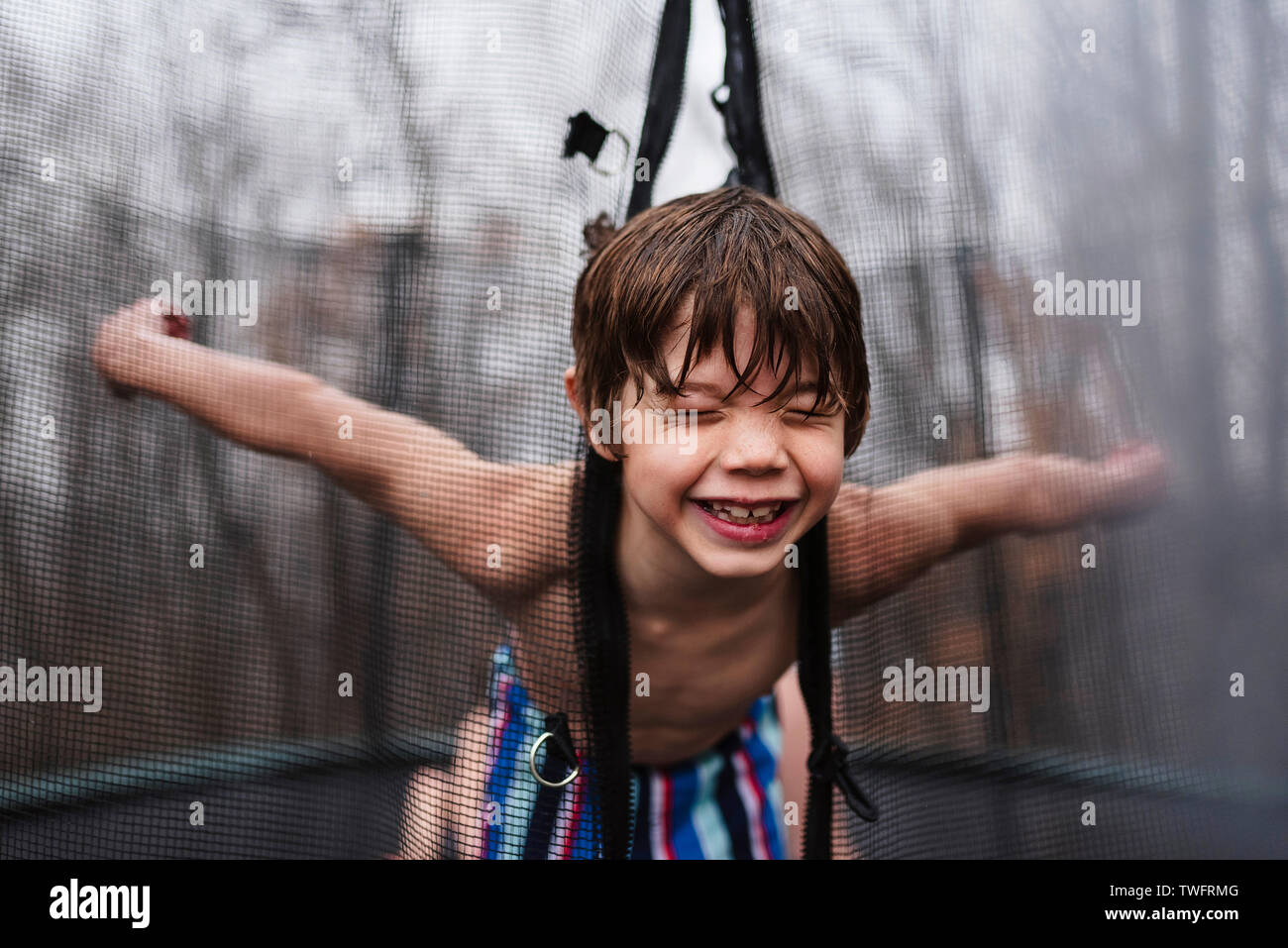 Happy boy playing on a trampoline in the rain, United States Stock