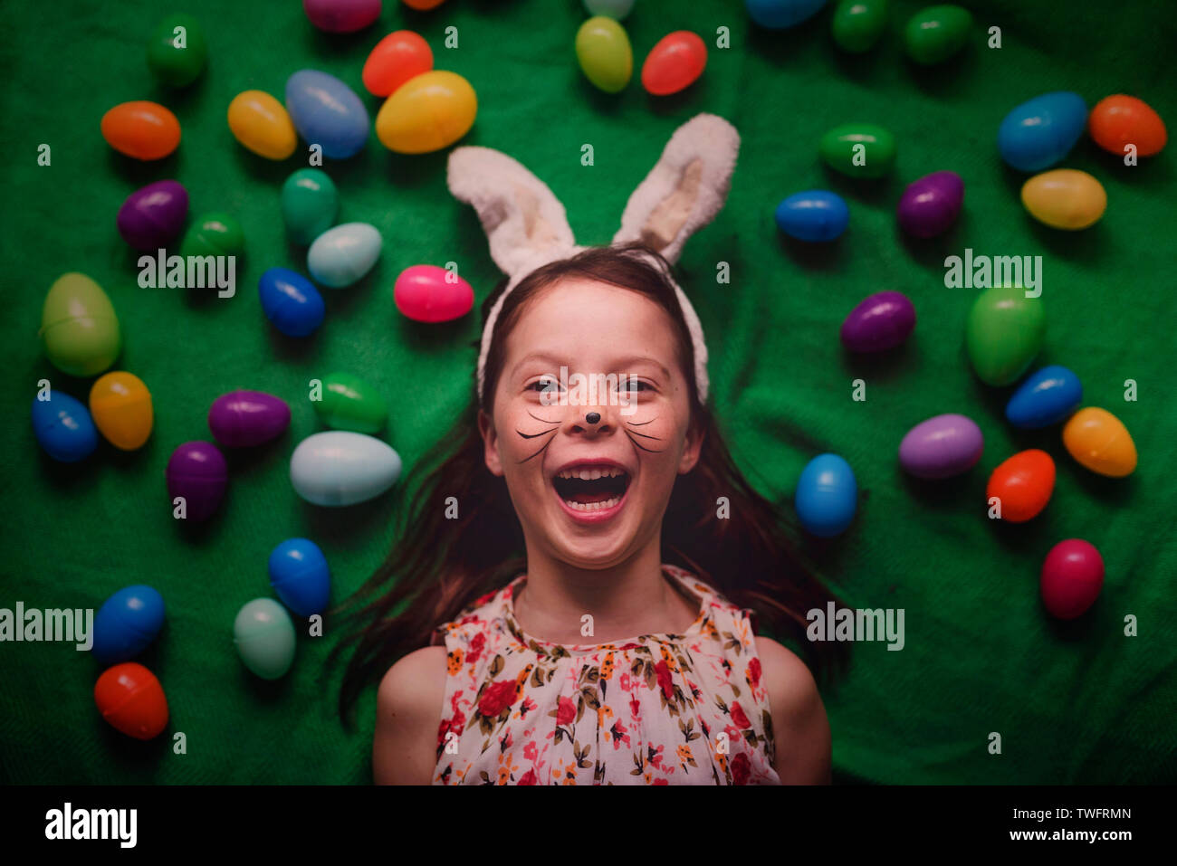 Overhead portrait of young girl wearing bunny ears surrounded by Easter eggs Stock Photo