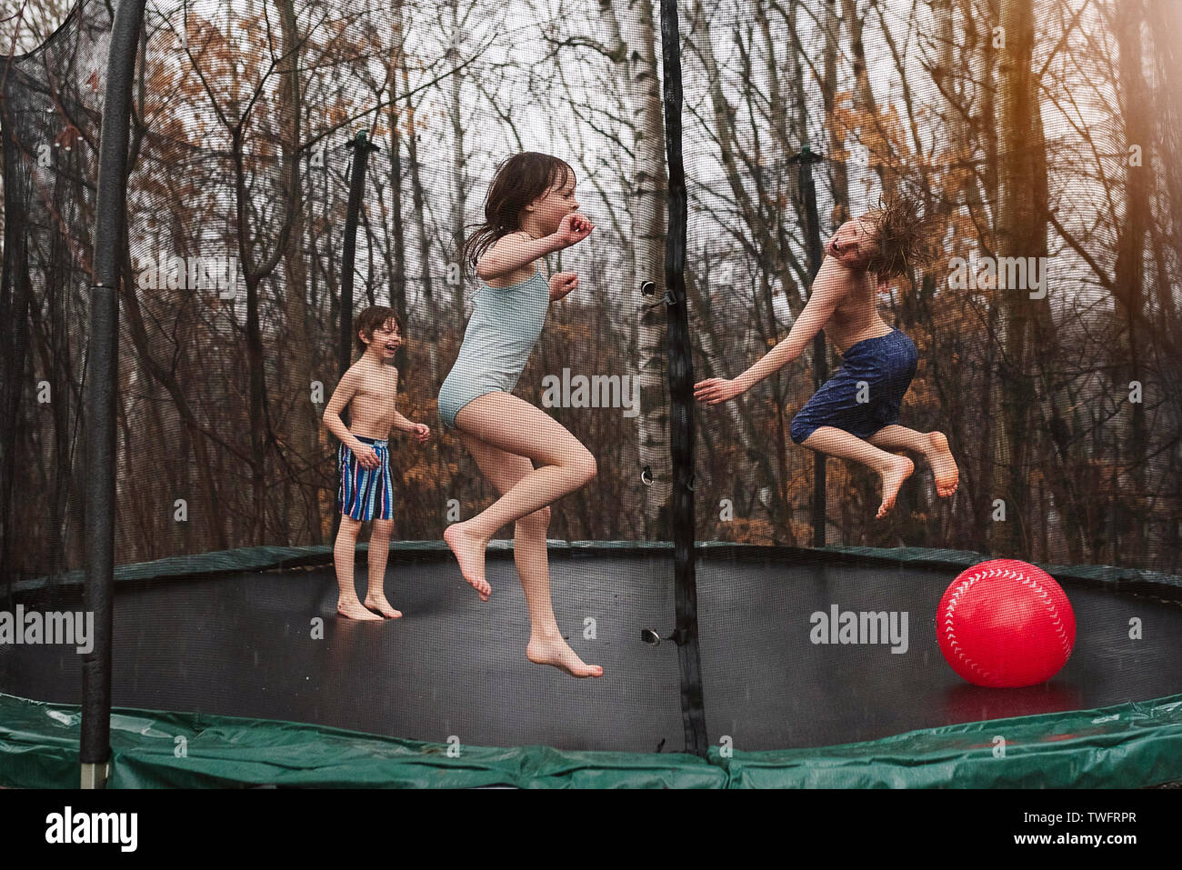 Three children jumping on a trampoline in the rain Stock Photo