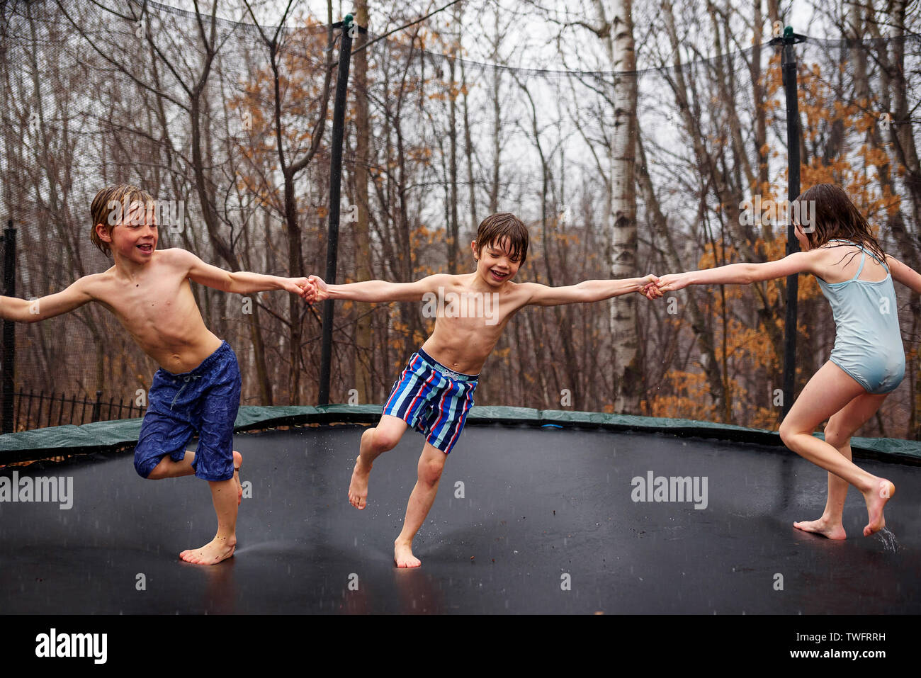 Three Children Jumping On A Trampoline In The Rain Stock Photo Alamy