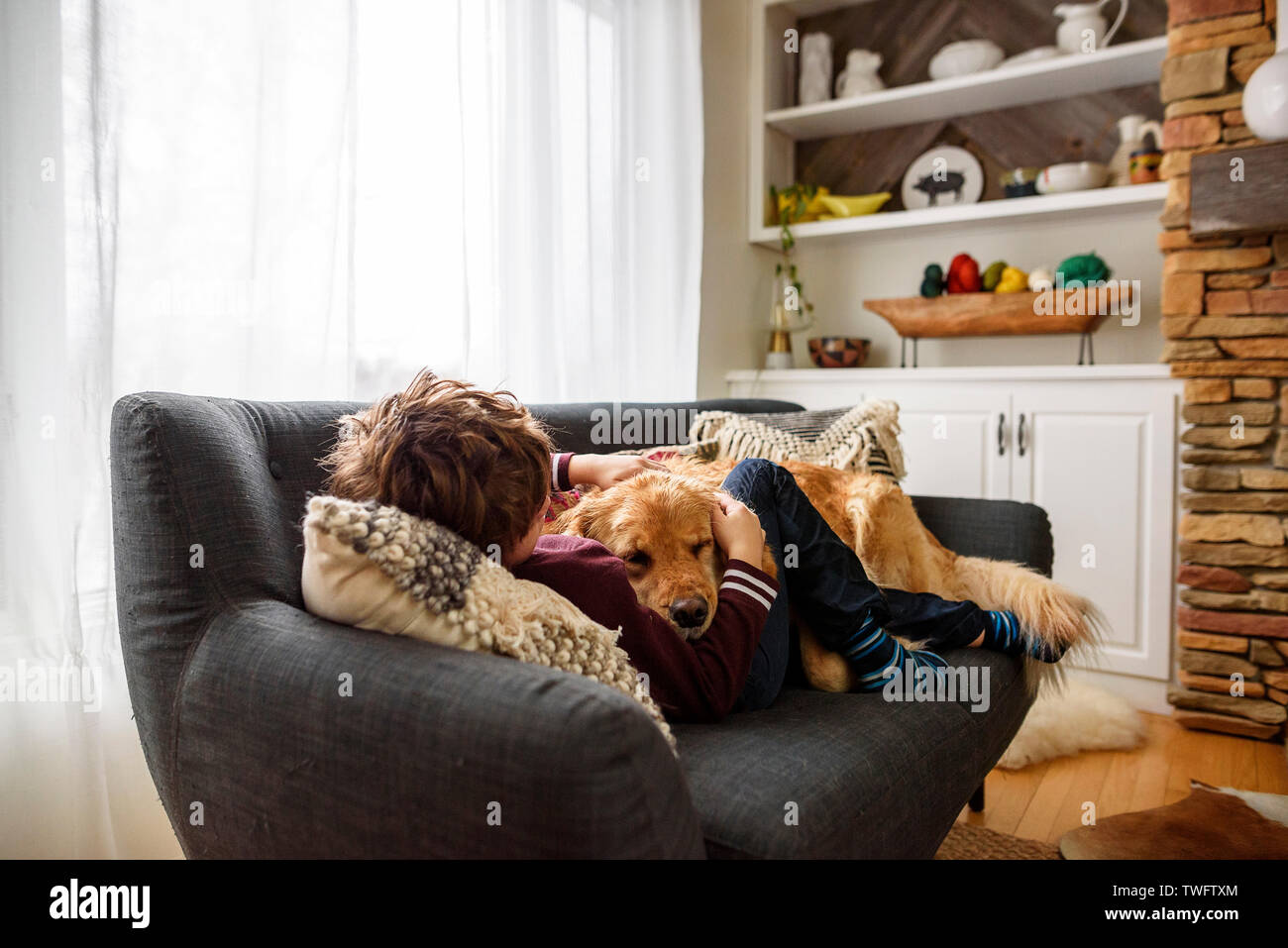 Boy lying on a couch cuddling a golden retriever dog Stock Photo Alamy
