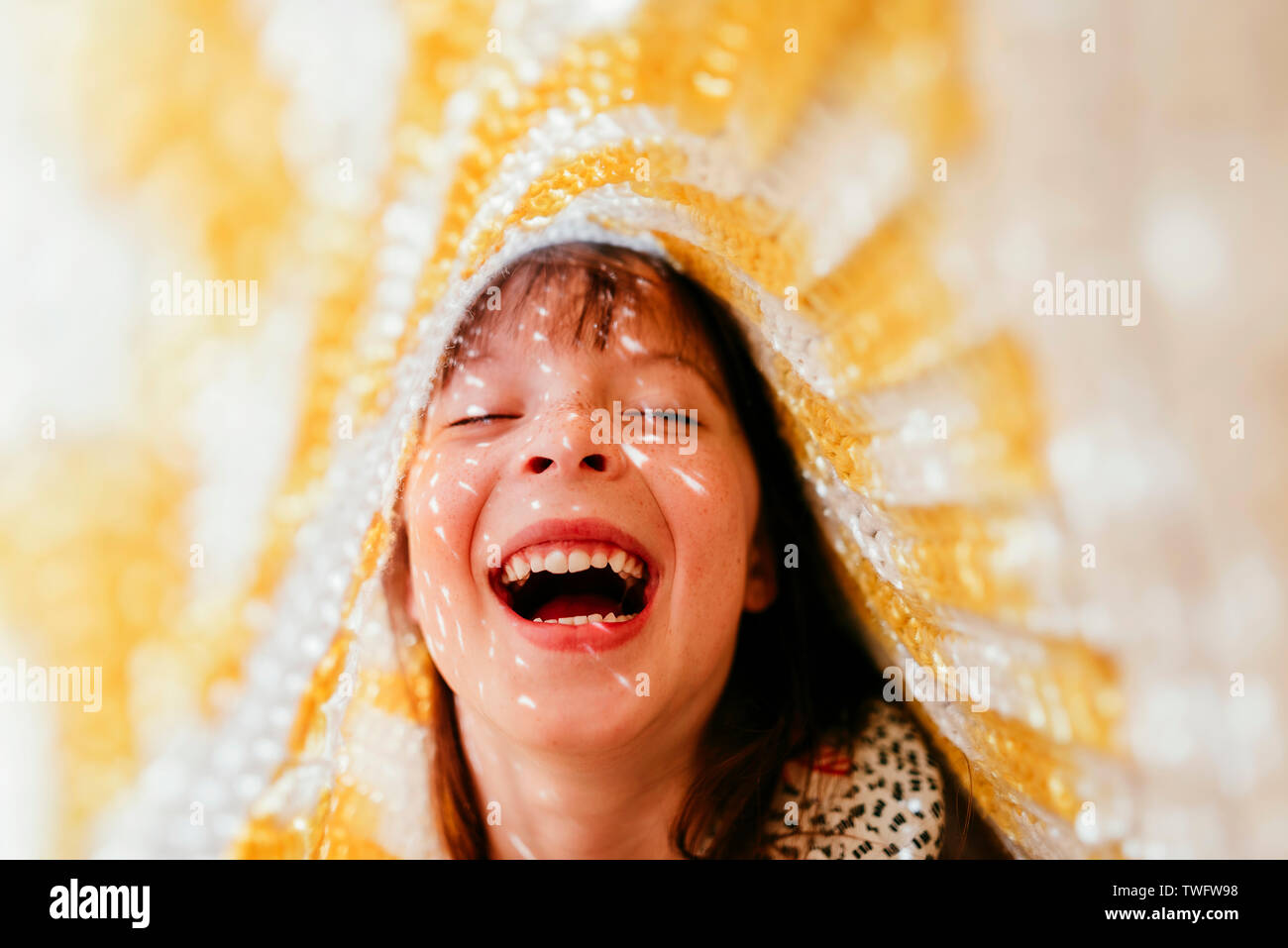 Portrait of a girl hiding under a blanket laughing Stock Photo