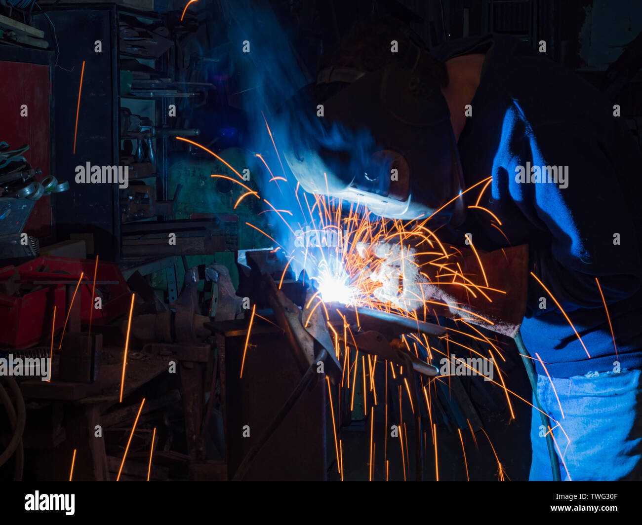 Metal working mechanic fabricator Technician MIG welding in a dark workshop with sparks flying shrouded in fumes Stock Photo