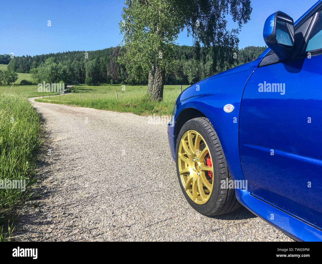 The blue youngtimer sports car with golden rims is standing on the narrow road and is ready to drive fast. Like being part of the rally. Stock Photo