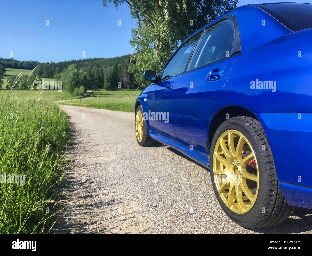 The blue youngtimer sports car with golden rims is standing on the narrow road and is ready to drive fast. Like being part of the rally. Stock Photo
