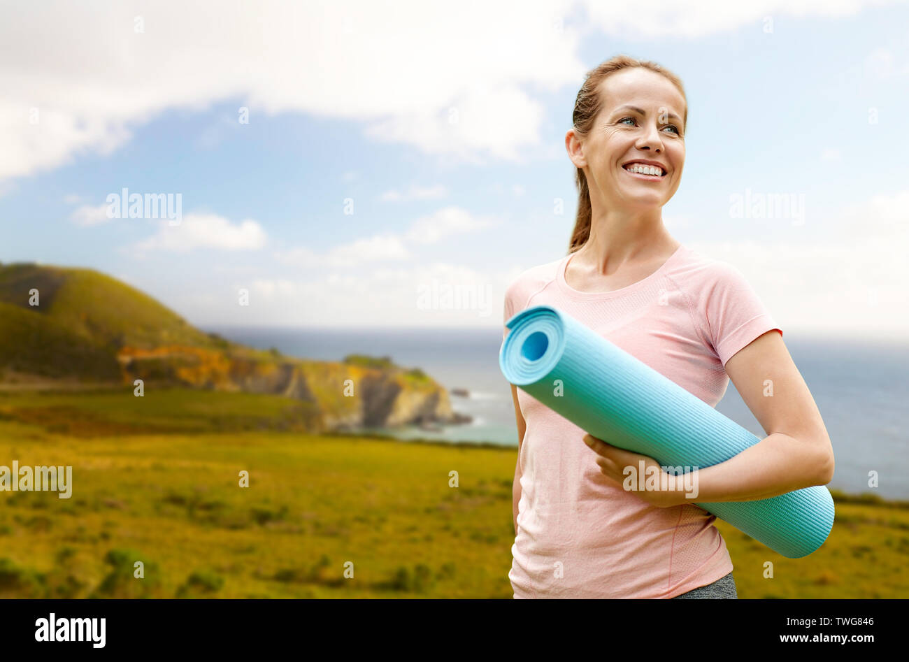 Mature happy middle aged woman 40s, long blond hair, smiling, big breasts,  in jeans, holding yoga mat, thermos in hands, against backdrop of European  architecture of residential area. body positivity Stock Photo