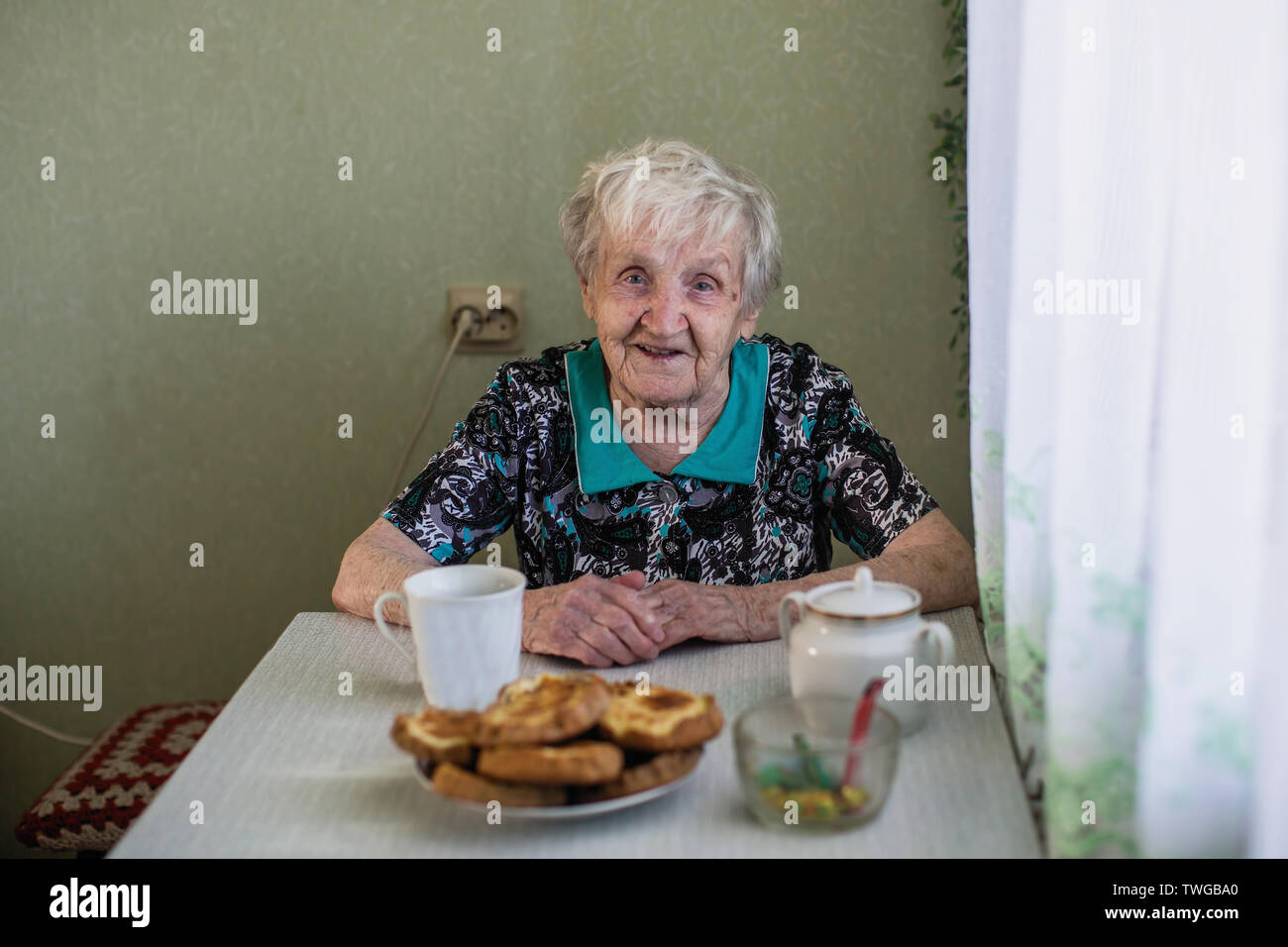 The old russian woman sitting at the kitchen table. Stock Photo
