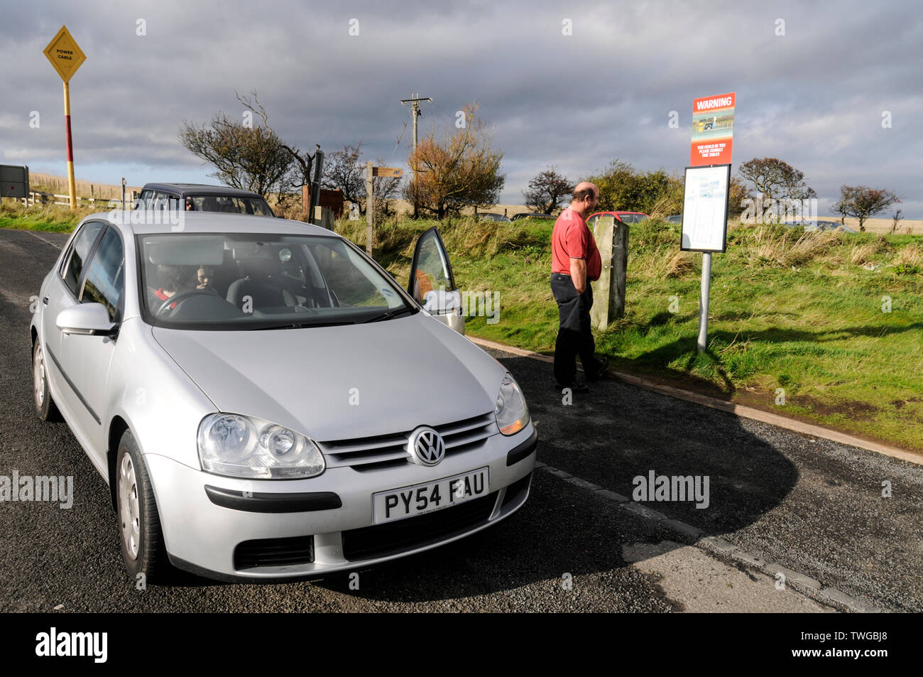 Visiting motorists stop to read the 'Tide Times' warning notices before crossing the causeway to Holy Island in Northumberland, Britain Stock Photo