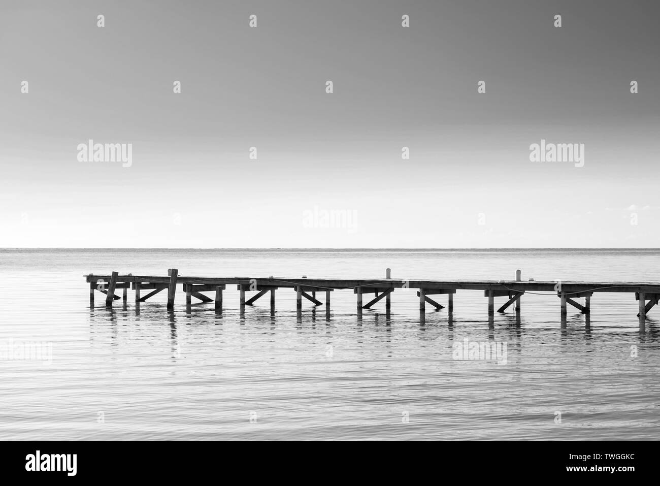 Wooden dock over calm ocean water as minimalism background in stunning black and white Stock Photo