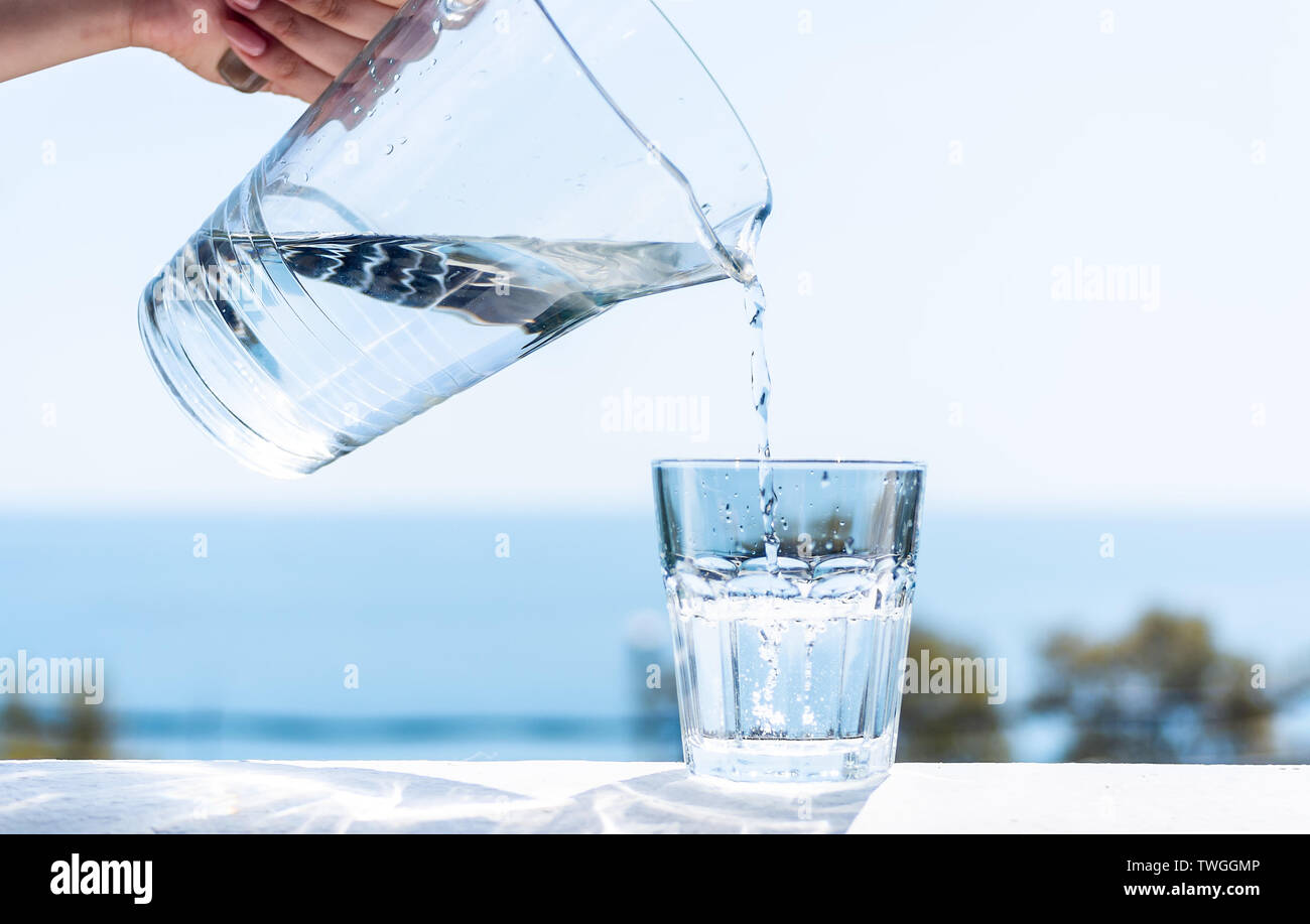 Purified water is poured from a glass jug into a glass. The concept of ...