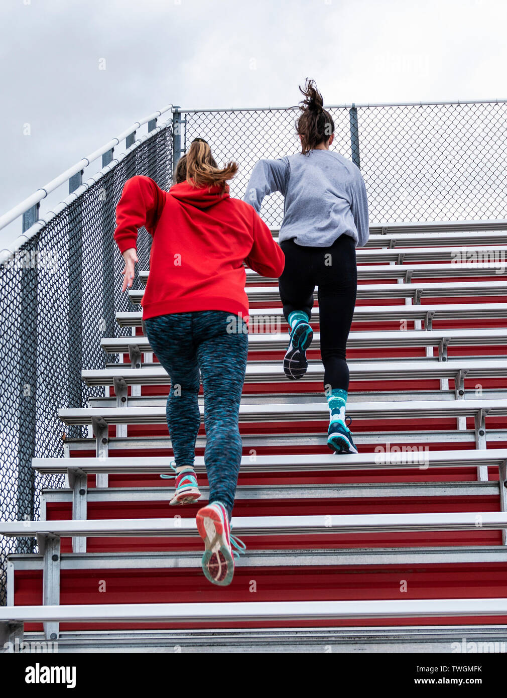 Two high school track and field runners are sprinting up red bleachers on a cloudy day at practice. Stock Photo
