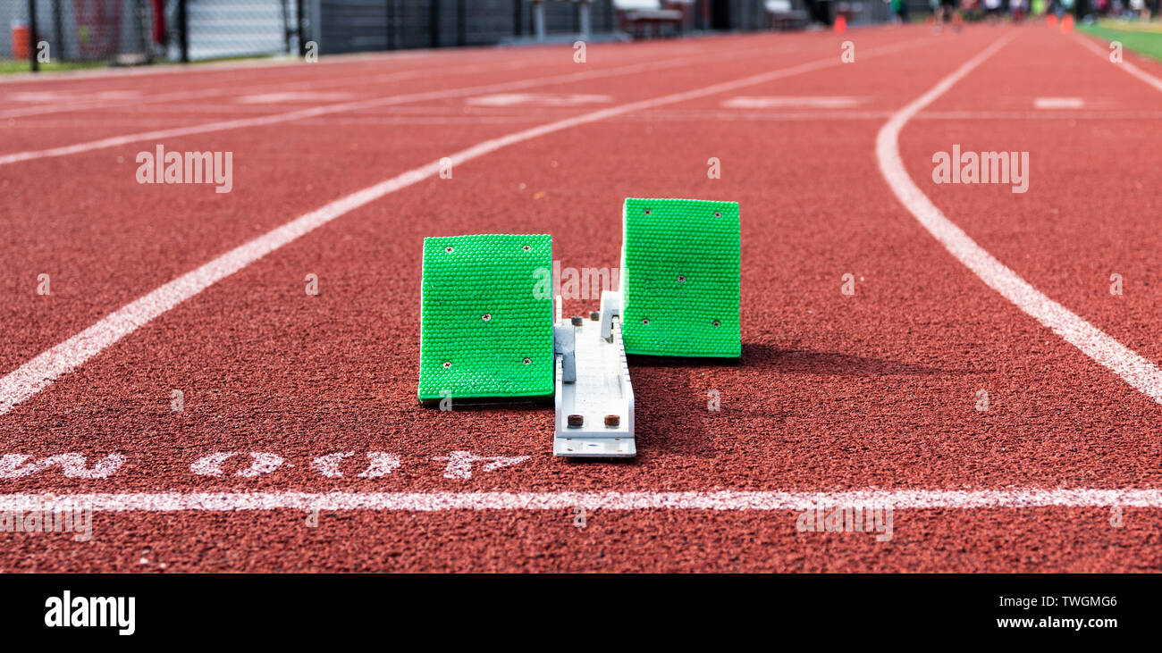 A set of green starting blocks are ready for a sprinter to run the 400 meter dash on a red track. Stock Photo