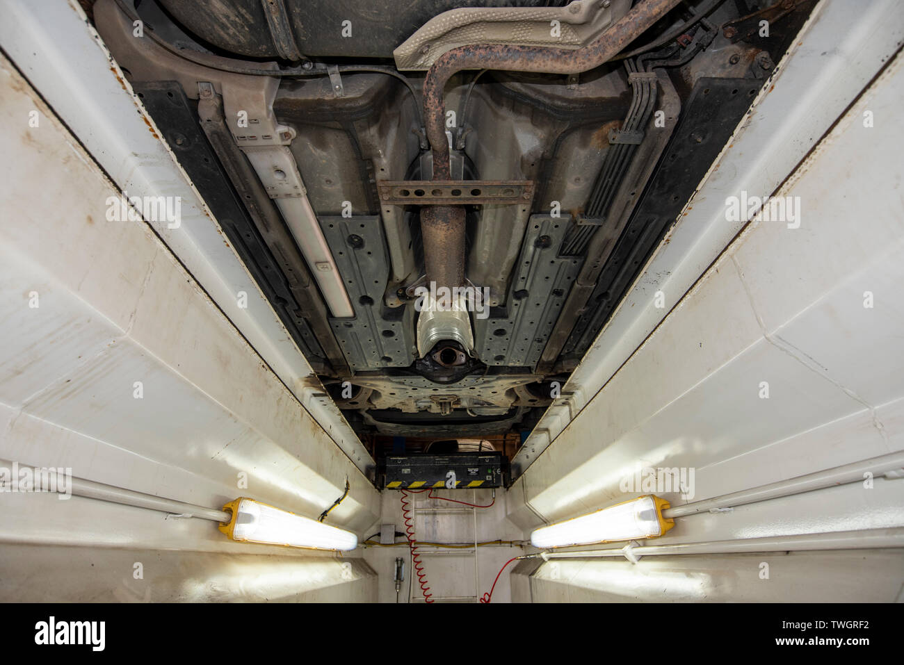 Toyota Prius Hybrid, stolen Catalytic Converter. Underneath vehicle from a mechanics inspection pit, showing location, missing and damaged components. Stock Photo