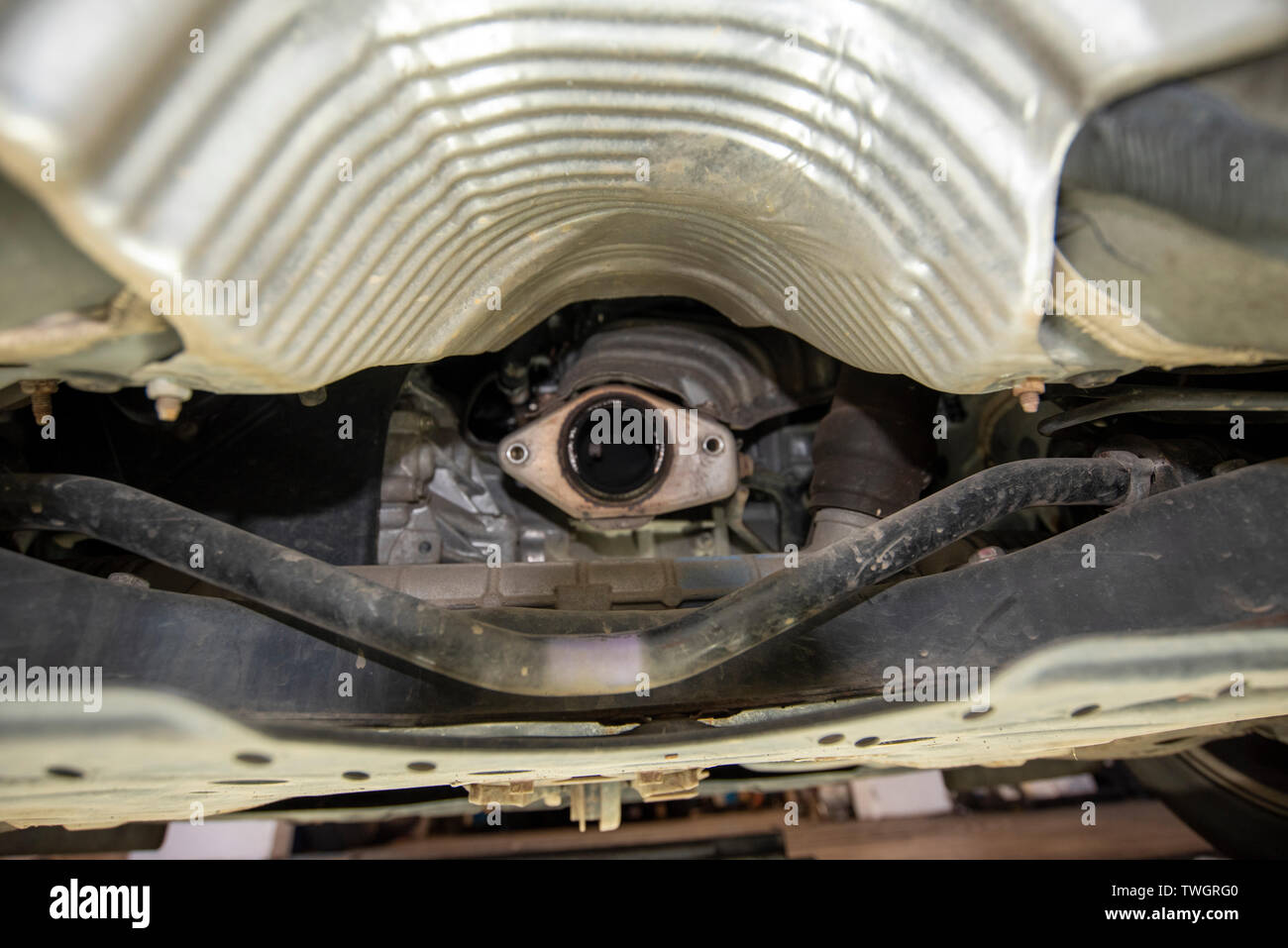 Toyota Prius, stolen Catalytic Converter. View underneath vehicle from a mechanics inspection pit, showing location of missing and damaged components. Stock Photo