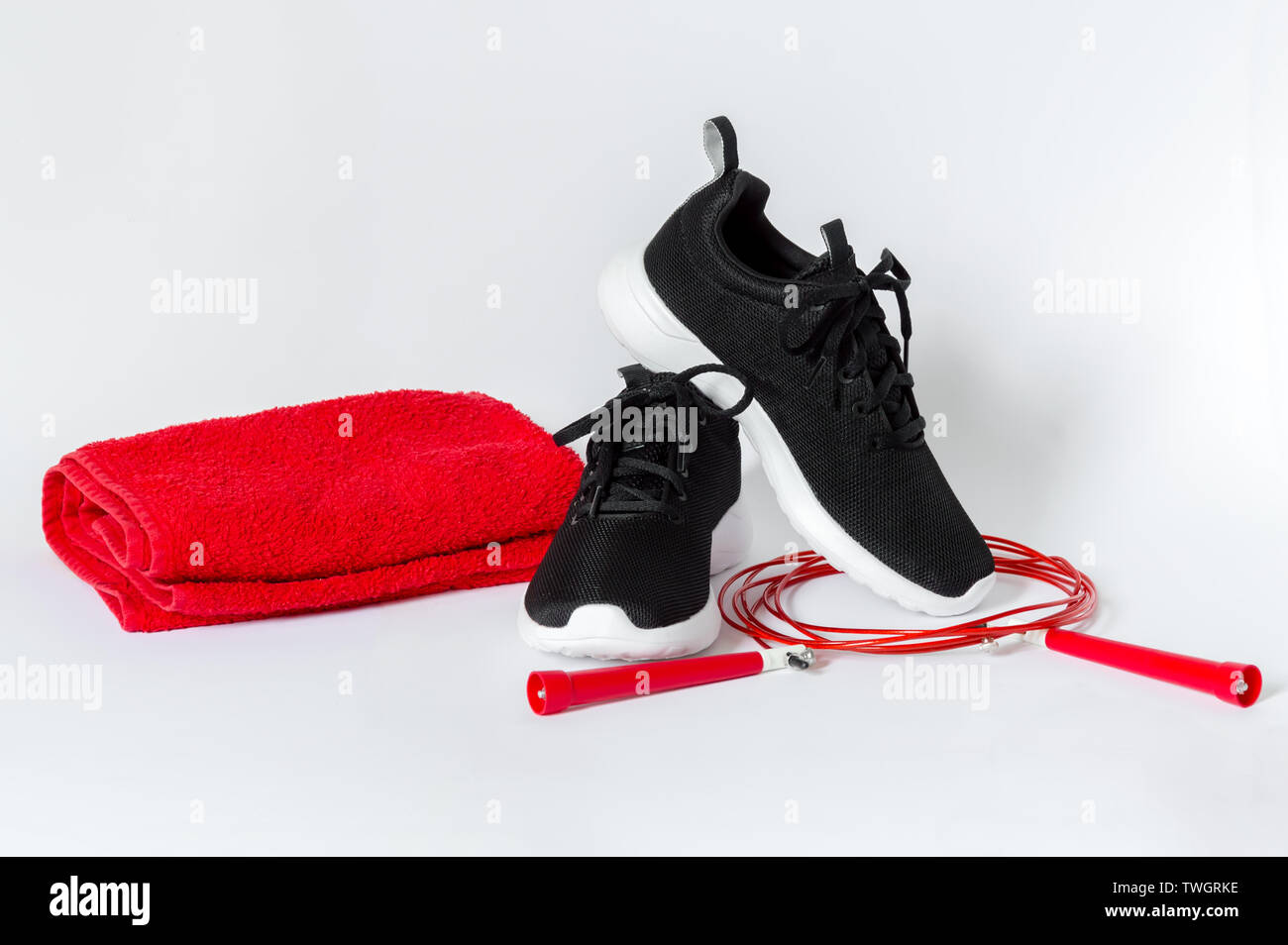 Black sports running shoes with white sole, red jumping rope and red towel isolated on white background. Concept of fitness and healthy lifestyle Stock Photo